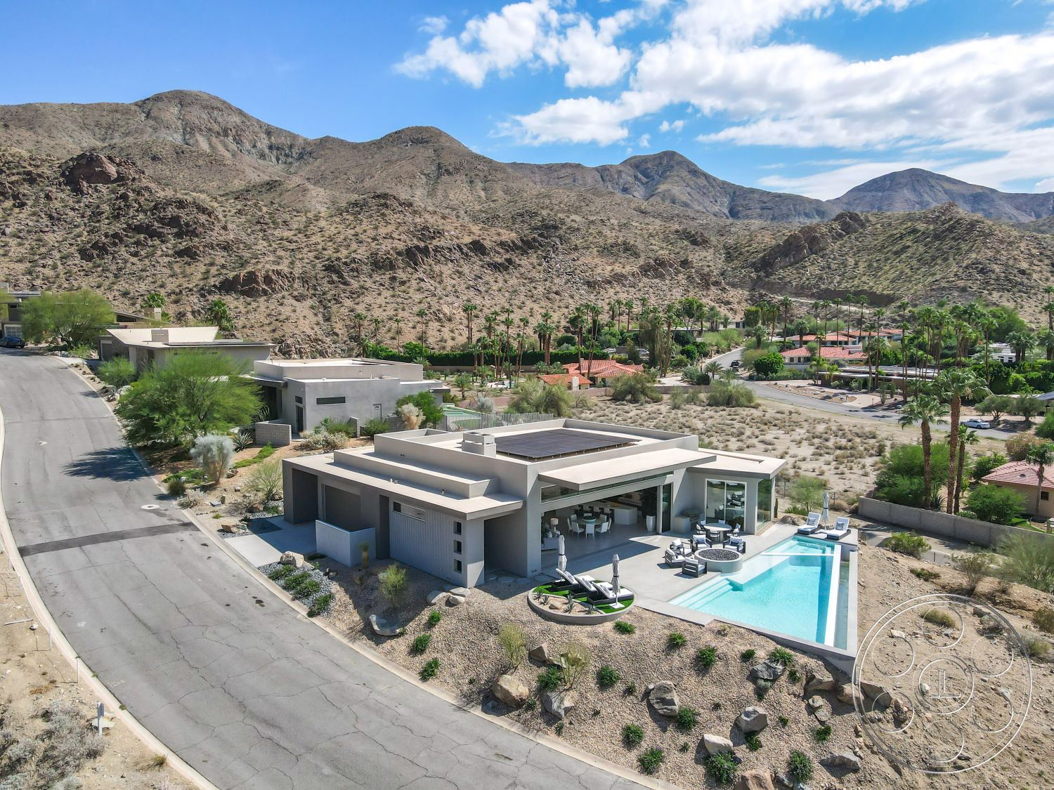 Palm Springs 109 - curved driveway, exposed concrete ceiling, concrete pool deck, glass patio doors, sliding glass walls, flat roof design, solar panel roof, open floor plan layout, landscaped garden beds, minimalist architectural style, exterior concrete walls, stone landscaping features, rectangular infinity pool, palm tree views, landscape lighting features, modern outdoor living space, desert mountain setting, tile flooring around pool area, urban desert villa, hardscape patio area, patio lounge furniture