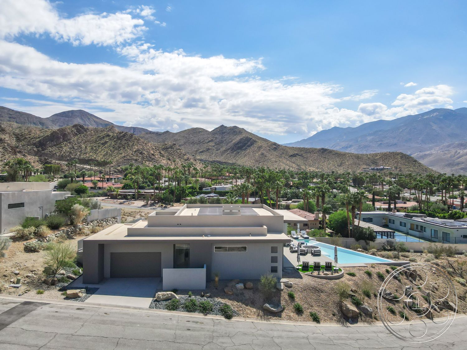 Palm Springs 109 - large glass windows, rectangular swimming pool, outdoor lounge area, modern architectural style, concrete driveway, poolside lounge chairs, hardscape patio, hardscape driveway, natural stone features, flat roof design, textured plaster wall, exterior concrete walls, minimalist outdoor design, exterior stone landscaping, landscaped garden areas, desert home setting, desert mountain view, open concept exterior spaces, patio with mountain backdrop, desert climate design elements