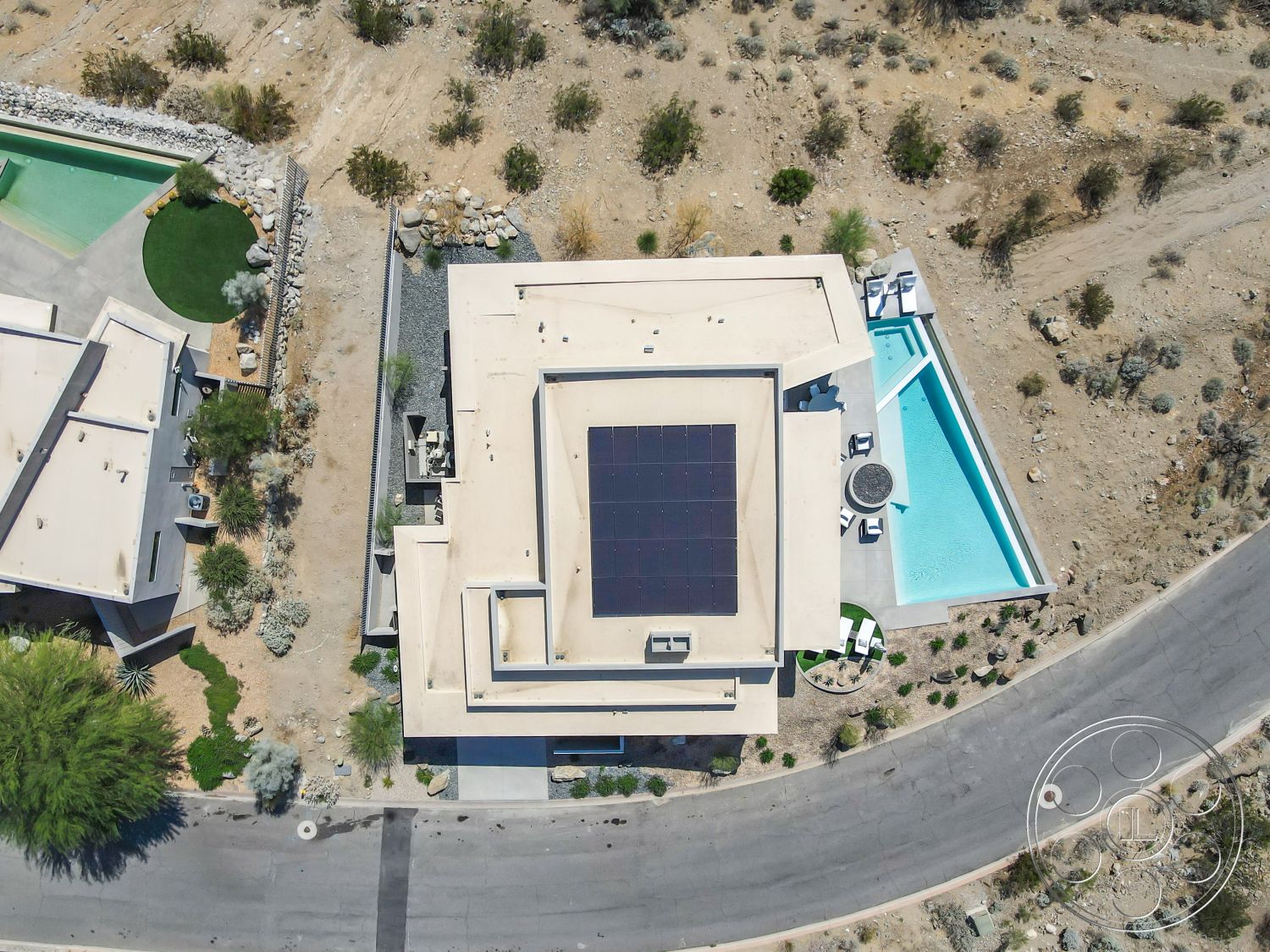 Palm Springs 109 - rectangular swimming pool, open outdoor space, concrete pool deck, surrounding desert flora, modern residential architecture, hardscape and softscape integration, curved driveway design, contemporary swimming area, flat roof design exterior, solar panel installation on roof, grass landscaping with stones, desert setting exterior, textured plaster walls exterior, minimalist interior layout, landscape stones border, family home exterior, adjacent green lawn, secluded neighborhood, circular patio area