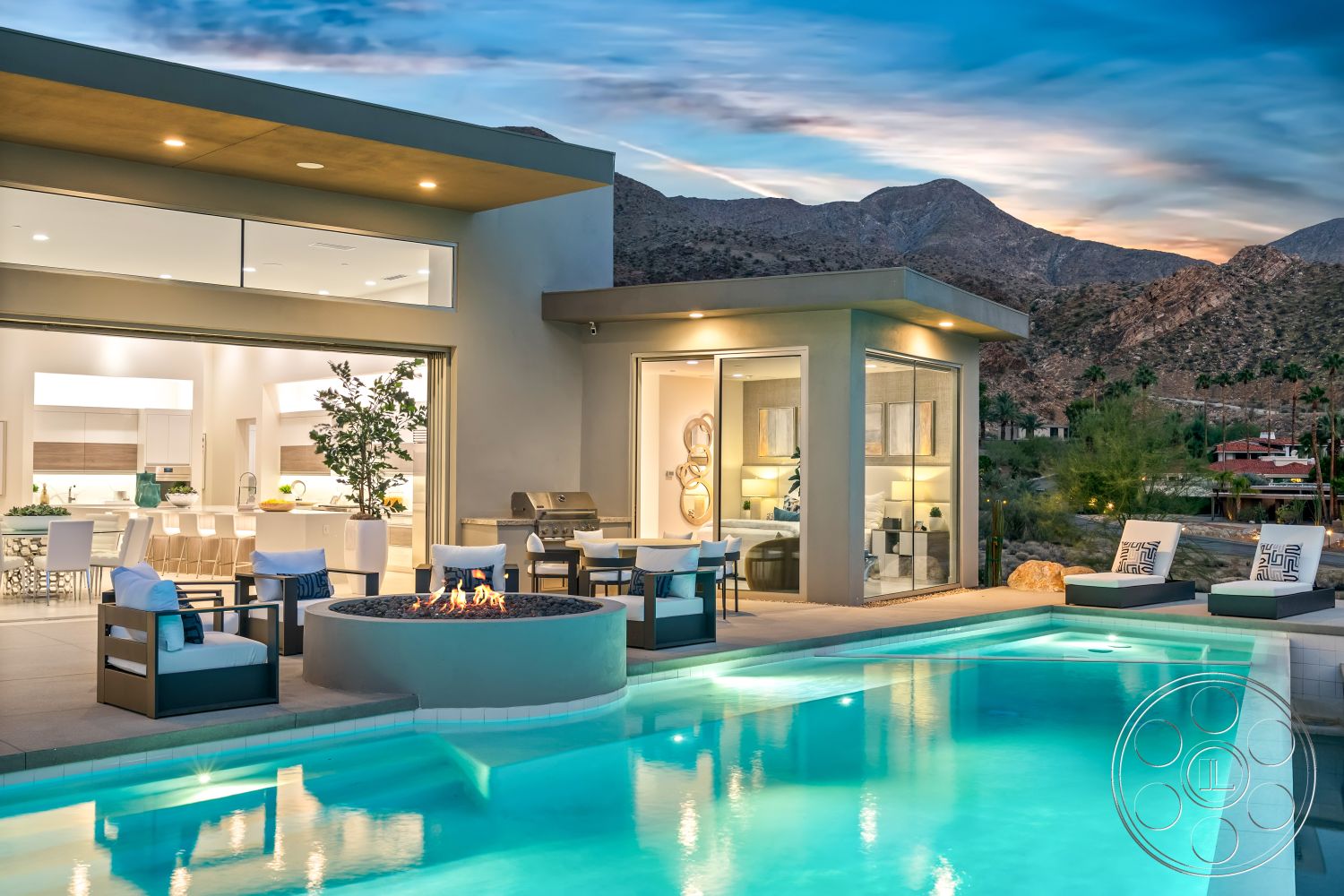 Palm Springs 109 - stone accent wall, sliding glass doors, modern outdoor furniture, mountain view, contemporary outdoor lighting, concrete pool deck, rectangular pool, wood dining chairs, stucco wall finish, open concept living area, floor-to-ceiling glass doors, porcelain tile flooring, landscaped patio area, interior modern kitchen, desert landscape setting, exterior swimming pool, fire pit lounge area, stone fireplace feature, aluminum grill station, modern aesthetic architecture