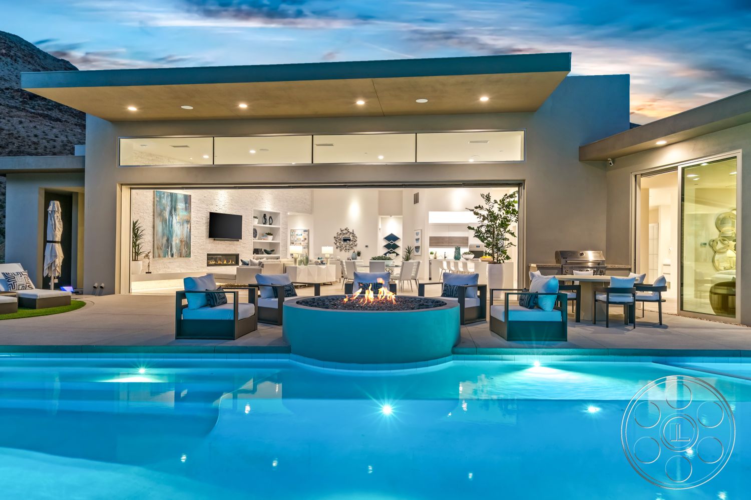 Palm Springs 109 - glass sliding doors, landscaped garden view, rectangular swimming pool, floor-to-ceiling windows, decorative wall art, smooth concrete pool deck, open concept living area, modern outdoor seating area, concrete patio floor, exposed stone feature wall, stainless steel outdoor grill, desert mountain setting, fire pit with circular stone border, interior living room with minimalist decor, ceramic tile kitchen backsplash, marble accent decor, wraparound patio design, luxury modern home, urban outdoor entertainment area, interior dining space with modern furnishings, exterior glass partition wall