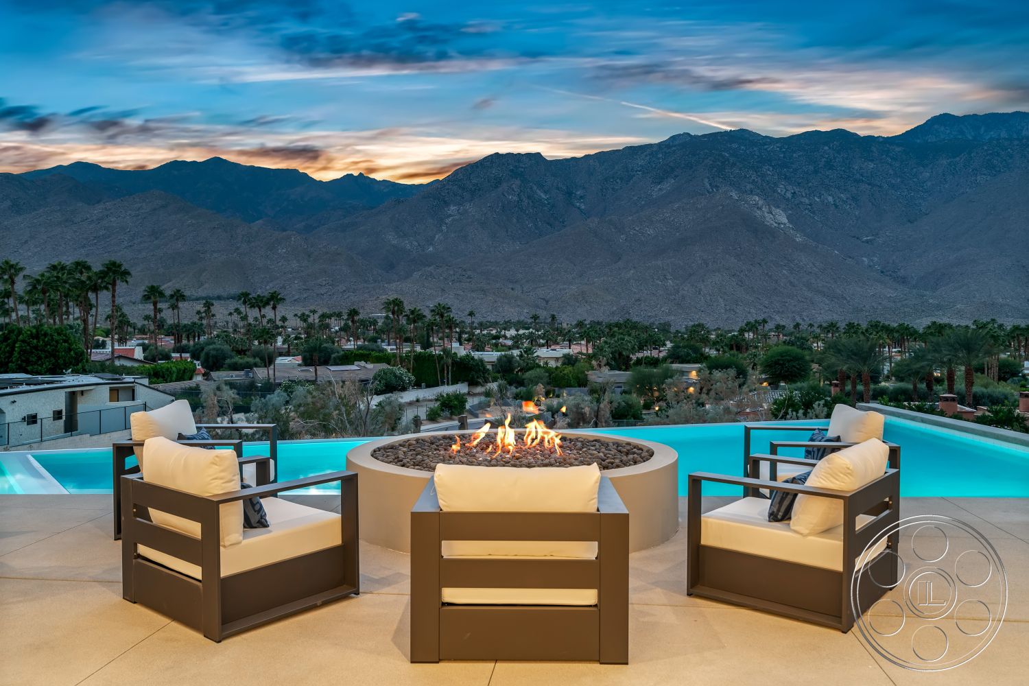 Palm Springs 109 - outdoor entertaining space, exterior seating area, textured concrete surface, luxurious outdoor retreat, contemporary architectural style, concrete patio flooring, minimalist outdoor design, palm tree landscape, rectangular infinity pool, mountain view backdrop, glass pool edge, modern fire pit with lava rock, aluminum outdoor chairs with cushions, open-air lounge with sunset view, surrounding desert environment, soft lighting with evening ambiance