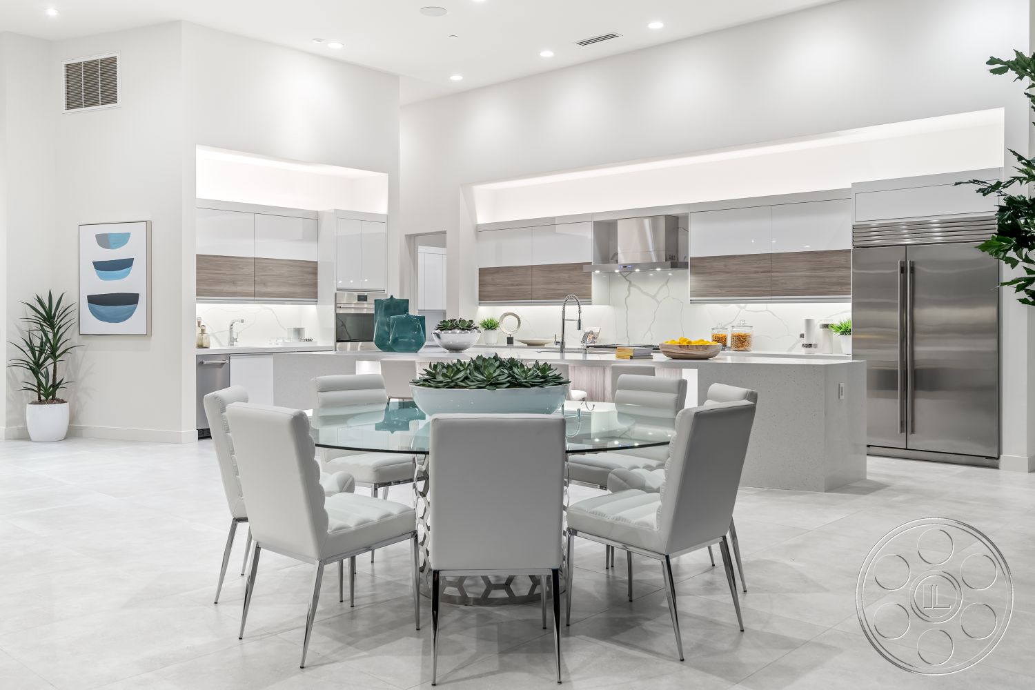 Palm Springs 109 - high ceilings, neutral color palette, open floor plan, minimalist design elements, round dining table, modern dining table, bright and airy space, recessed ceiling lights, stainless steel kitchen appliances, glass kitchen backsplash, quartz kitchen countertops, built-in storage solutions, low-maintenance indoor plants, smooth plaster walls, contemporary home decor, island kitchen with seating, white leather dining chairs, ceramic tile kitchen floors, white cabinetry with wooden accents, fridge with stainless steel finish, accent wall with art