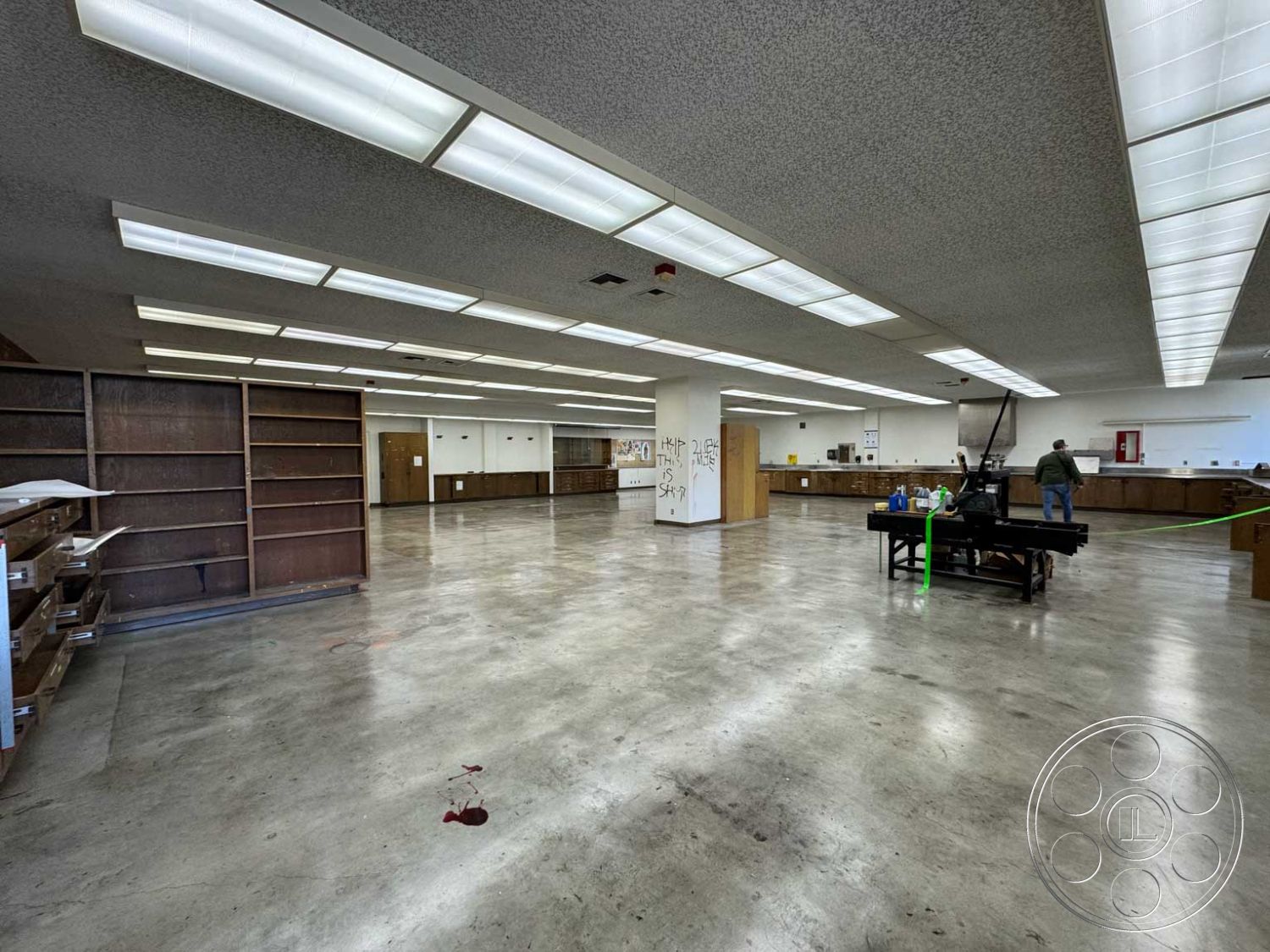 School 3 - open space layout, industrial style, neutral wall color, wall-mounted shelving, multipurpose room, unfinished interior, textured acoustic ceiling tiles, exposed concrete flooring, commercial space interior, flourescent panel lighting, laminated wood cabinetry