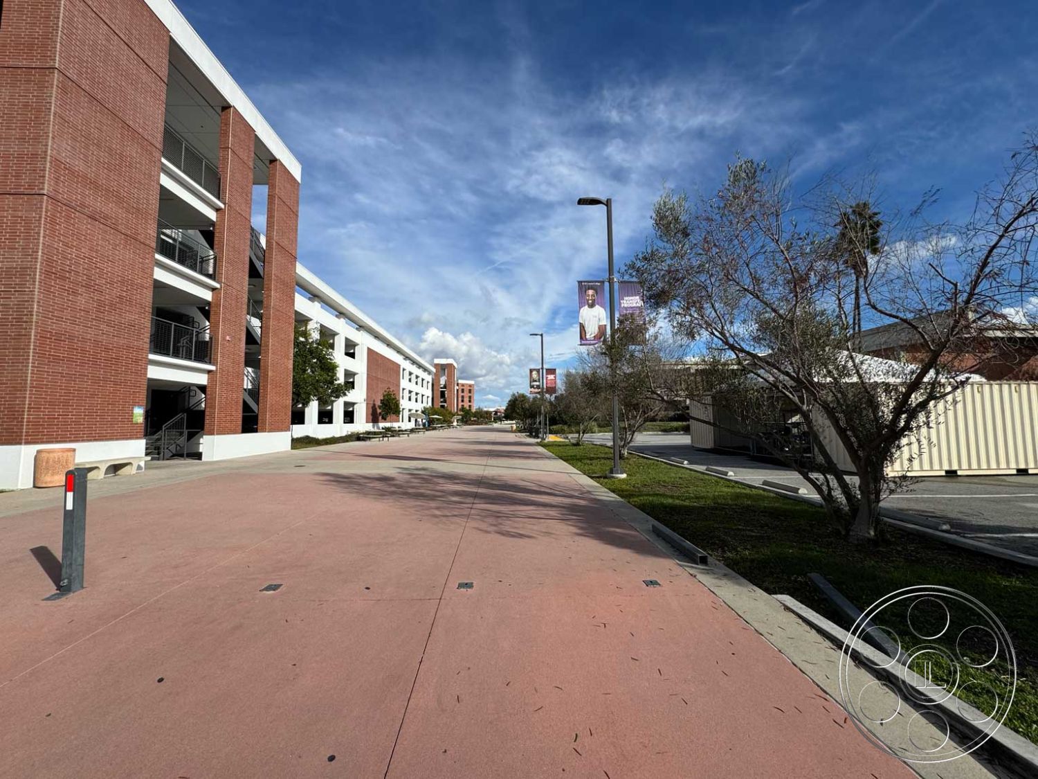School 3 - open space design, urban landscape, modern architectural style, paved parking lot, landscaped green areas, metal stair railings, exterior brick facade, concrete pedestrian walkway, integrated signage, multi-level parking structure, sunny sky backdrop, banners on lamp posts, rectangular building shapes