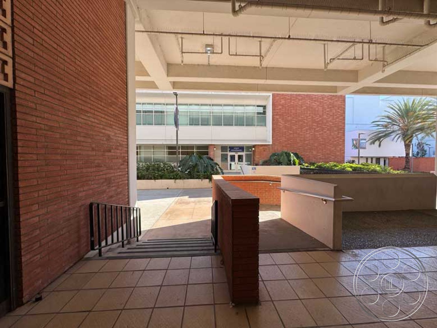 School 3 - urban setting, open courtyard, stainless steel railings, exposed concrete ceiling, commercial building design, exterior brick walls, modern glass windows, landscaped entrance area, green foliage landscaping, tiled entrance floor, pedestrian access steps, paved exterior pathway, rectangular building layout, concrete ramp for accessibility, sunlit entranceway