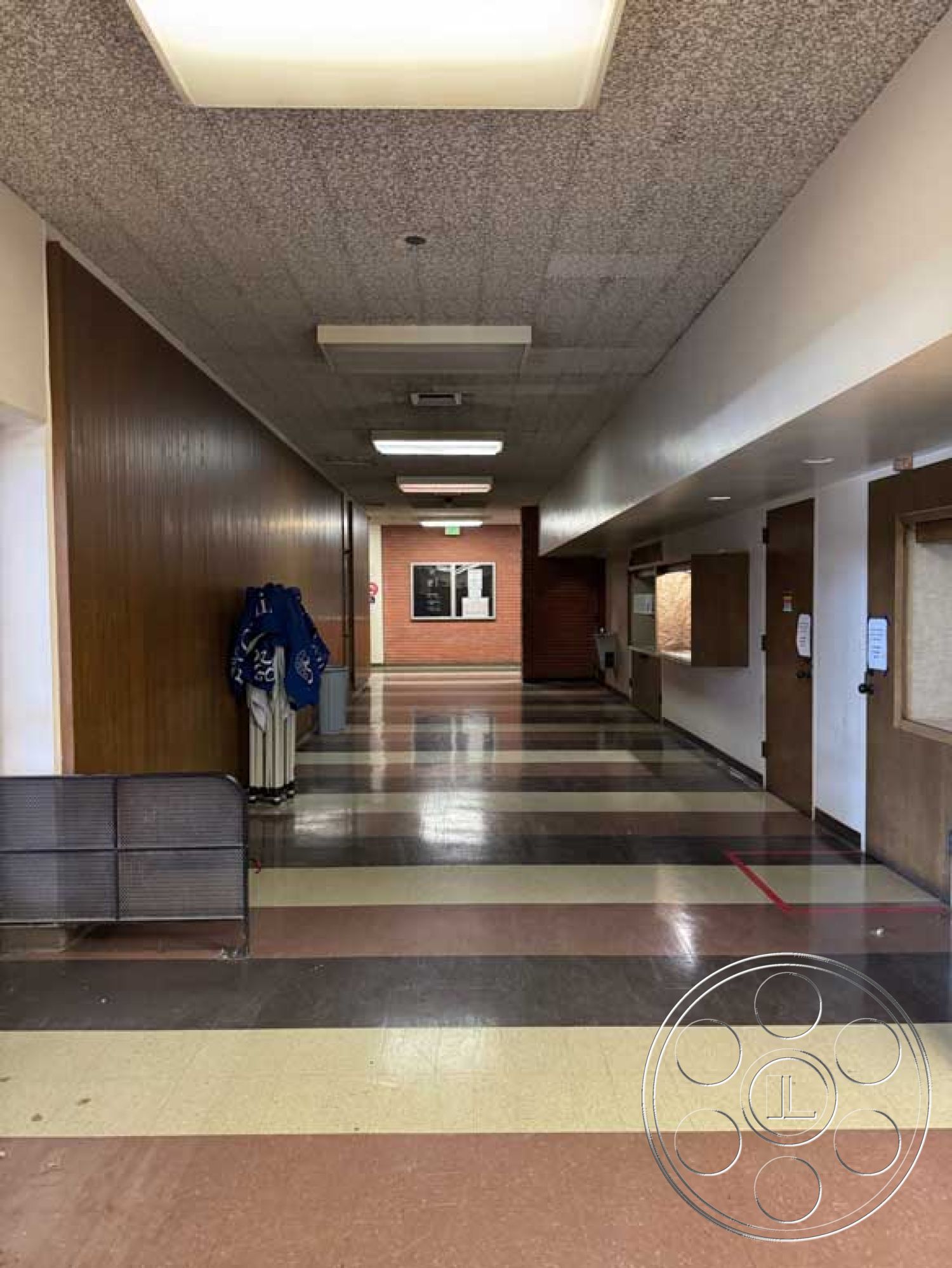 School 3 - minimalist design elements, industrial style, clean lines architecture, textured acoustic ceiling tiles, interior corridor space, wooden door frames, fluorescent overhead lighting, rectangular hallway layout, wood paneled wall cladding, black and white checkered vinyl flooring, plastered wall surface, straight hallway, metallic rail barrier, brick wall accent