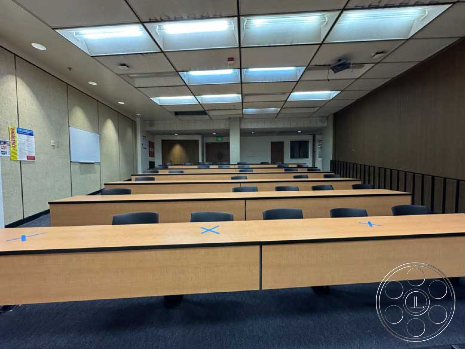 School 3 - vinyl flooring, acoustic ceiling tiles, painted drywall walls, interior classroom setting, projector mounted on ceiling, laminate lecture tables, black mesh office chairs, fluorescent panel lighting, large whiteboard, multimedia presentation area, divider railing at back, sectioned seating arrangement
