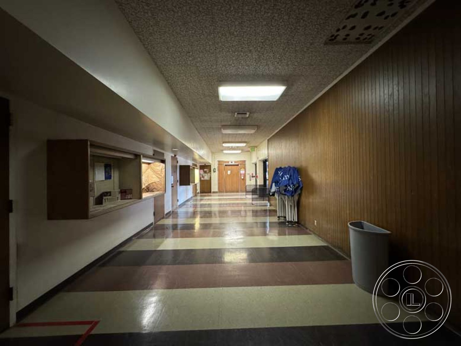 School 3 - neutral color palette, brown wooden door, interior corridor, textured acoustic ceiling tiles, wood paneling wall treatment, black and white checkered tile floors, flush-mounted LED ceiling lights, built-in wooden display counter, red striping floor design, metal trash can, hanging coat rack, public building hallway