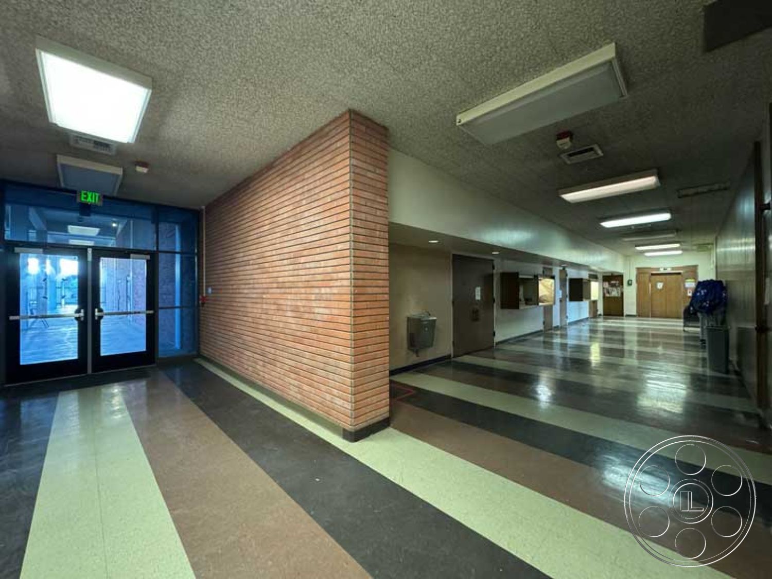 School 3 - open corridor layout, exterior brick wall, glass entry doors, drop ceiling with fluorescent lighting, interior tile hallway flooring, striped vinyl flooring, exposed aggregate ceiling, wall-mounted water fountain, wood panel classroom doors, access points for hallway circulation