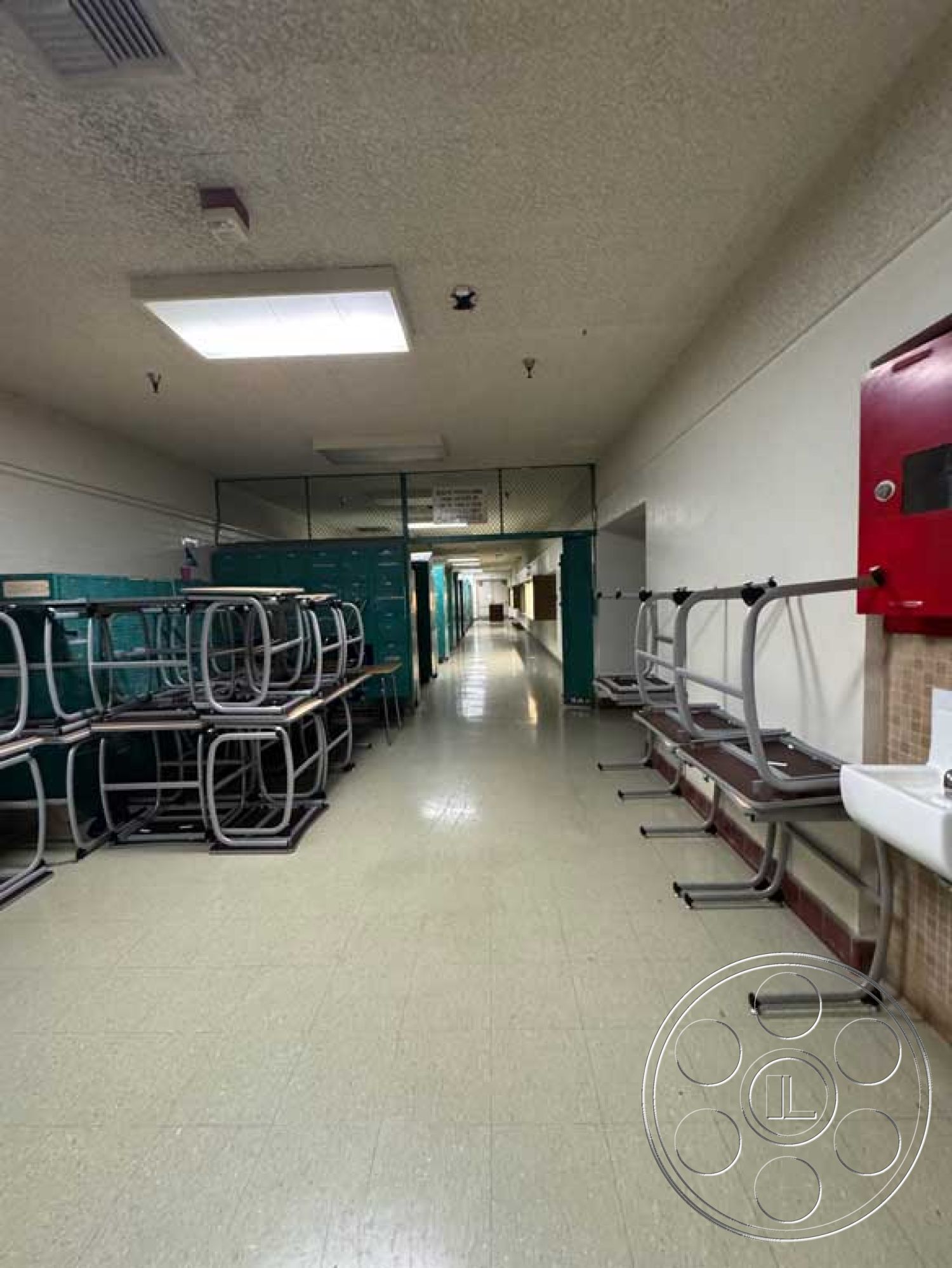 School 3 - metal lockers, white painted walls, minimalist architectural style, clear sight lines, fluorescent ceiling lights, linoleum flooring hallway, stacked cafeteria tables, exposed ceiling with HVAC vents, faux marble countertop sink, school corridor interior, functional educational environment, safety railing, red fire alarm box, public building design