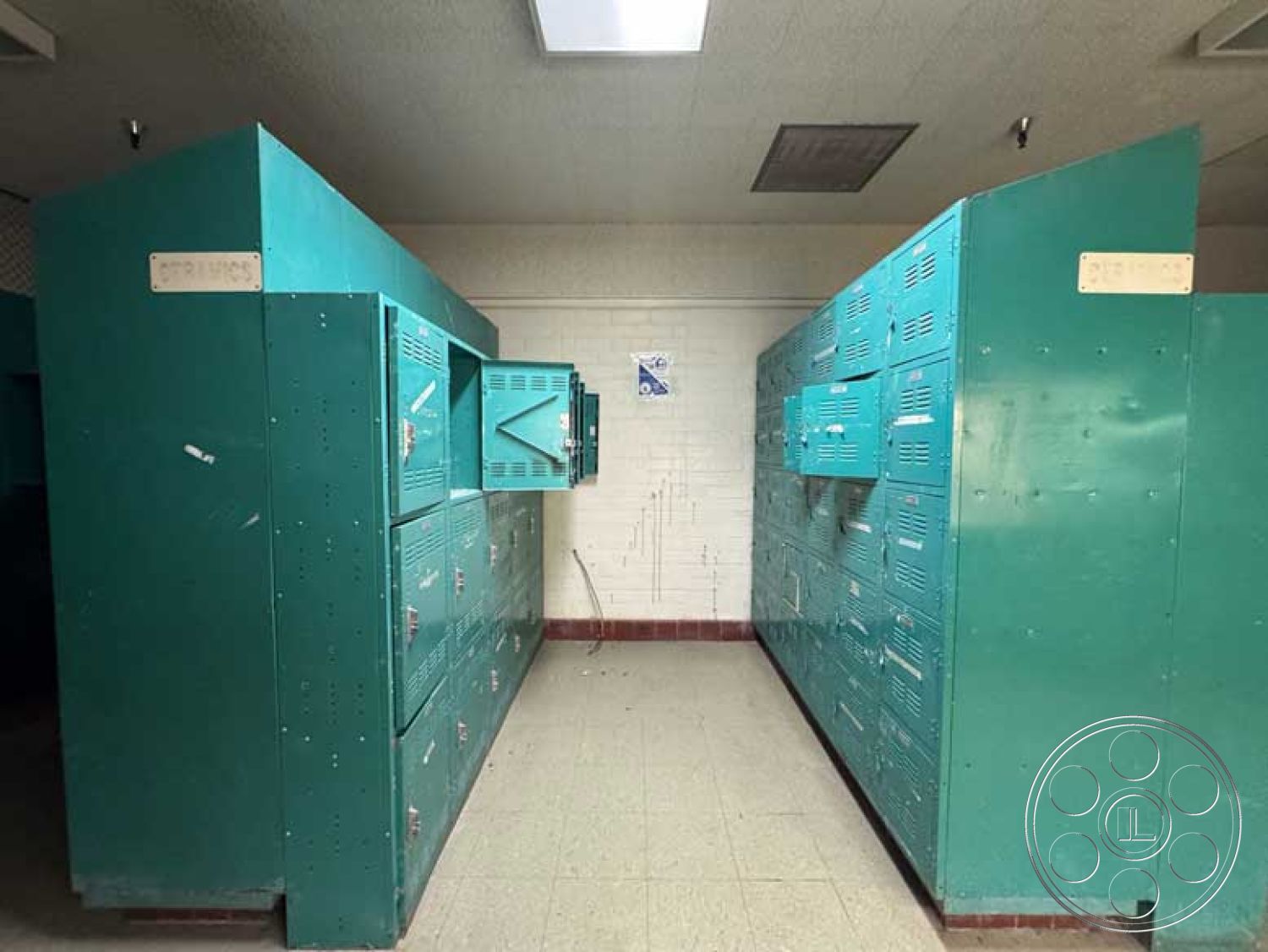 School 3 - exposed ceiling lights, square room layout, white painted brick walls, metal lockers interior, vintage teal locker units, industrial locker room design, split locker setup, metal storage compartments, tile floor flooring, commercial space architecture