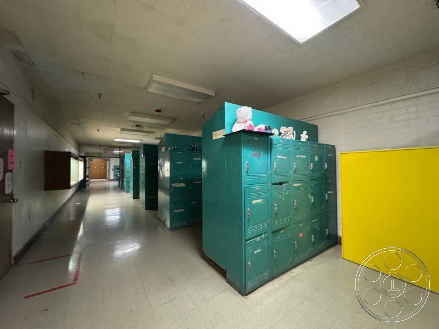 School 3 - open space layout, brick wall accents, metal lockers, interior hallway, yellow accent wall, drop ceiling with fluorescent lighting, green metal locker units, tile hallway flooring, empty school corridor, plastic storage bins on lockers, childhood memorabilia display
