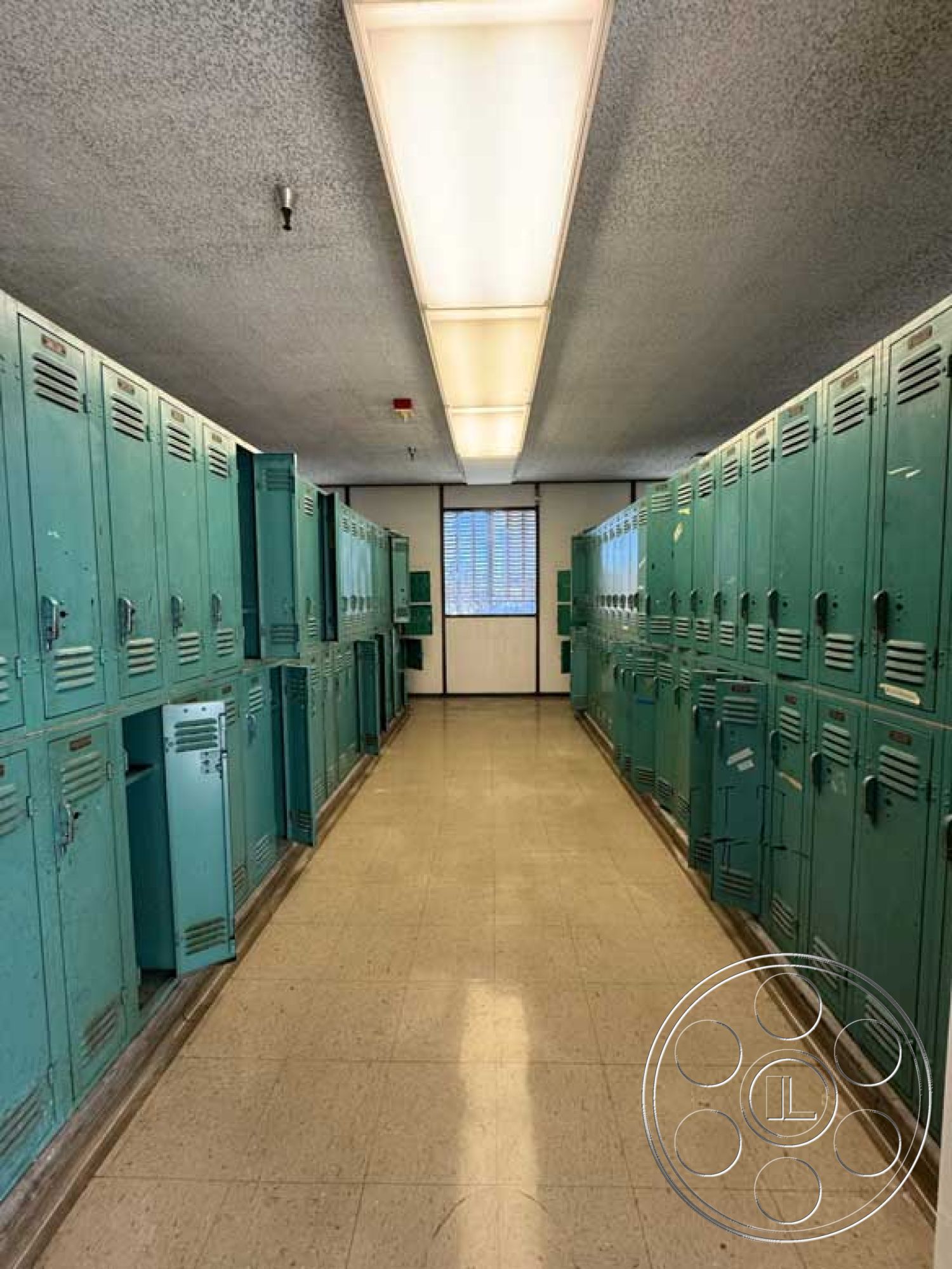School 3 - vinyl flooring, overhead lighting fixtures, plain walls, fluorescent ceiling lights, narrow hallway layout, metal lockers interior, green painted locker storage, large window with blinds, industrial school locker room, functional storage design, minimalist corridor, retro locker aesthetic, tile baseboard, metal door handles, open locker compartments, uniform locker arrangement