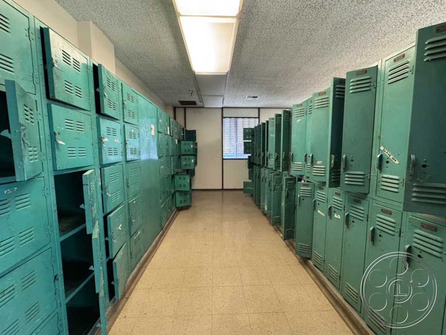 School 3 - industrial style, long corridor, windows with blinds, metal lockers, fluorescent ceiling lights, open storage space, textured acoustic tile ceiling, green painted lockers, perforated locker doors, vinyl floor tiles, interior locker room
