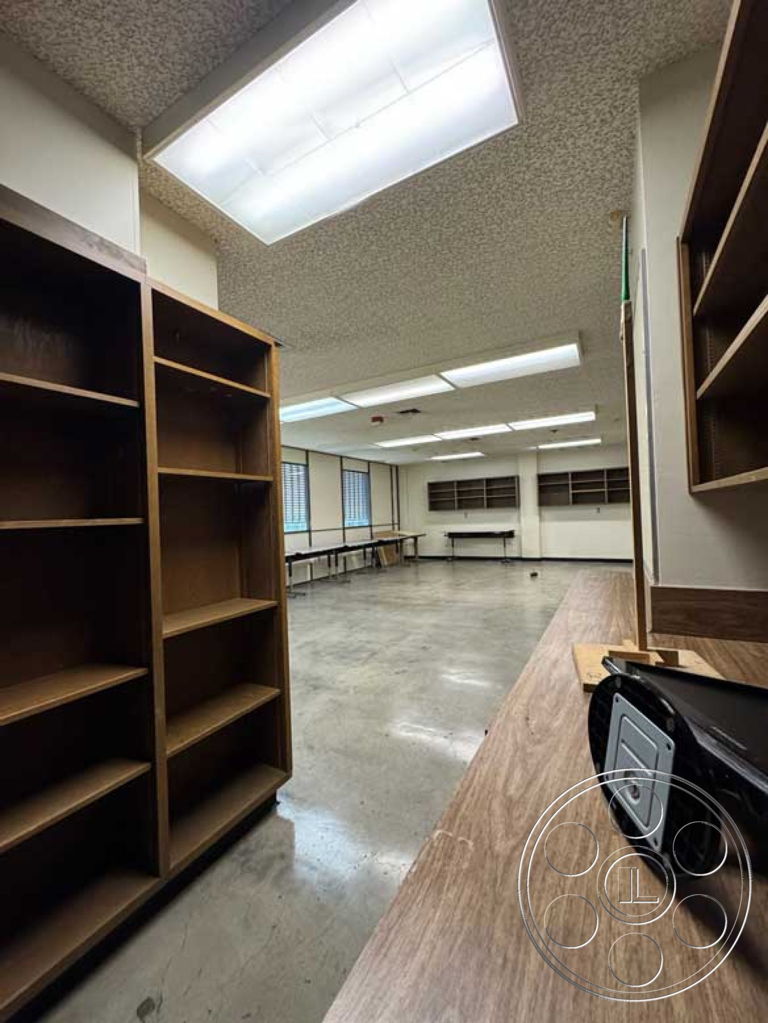 School 3 - large windows, open layout, concrete flooring, interior space, wooden shelving units, exposed ceiling tiles, industrial-style lighting, laminate countertop, rectangular room, temporary workspace, moderate natural light