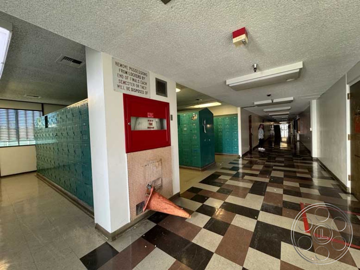 School 3 - exposed concrete walls, interior hallway, emergency exit signage, long corridor layout, fluorescent ceiling lighting, glossy black and white checkered tile floors, metal green school lockers, fire alarm system, painted wall signage, vinyl window frames, louvered windows for ventilation, open educational space, functional school architecture, public facility design