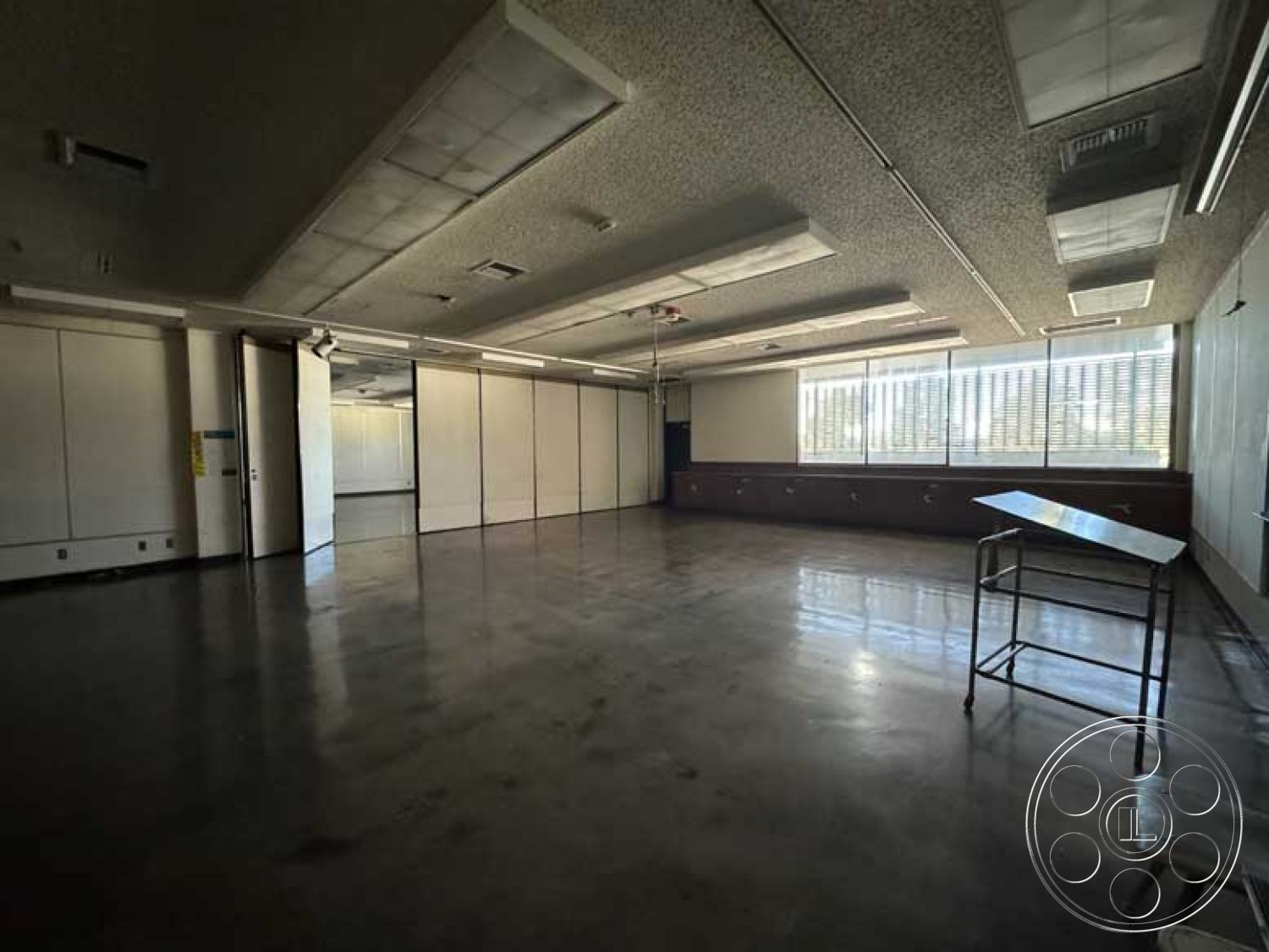 School 3 - minimalist design, neutral wall colors, polished concrete floors, functional workspace, industrial lighting fixtures, exposed ductwork, drop ceiling panels, large windows with blinds, open classroom layout, custom cabinetry wall, folding partition walls, marble tabletop