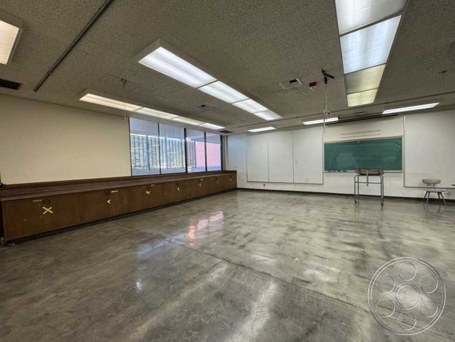School 3 - flat ceiling, plain white walls, educational environment, exposed concrete flooring, industrial ceiling design, interior classroom space, fluorescent ceiling lighting, teacher's desk area, laminate wooden cabinetry, wall-mounted whiteboard, tall windows with metal frames, straight classroom layout