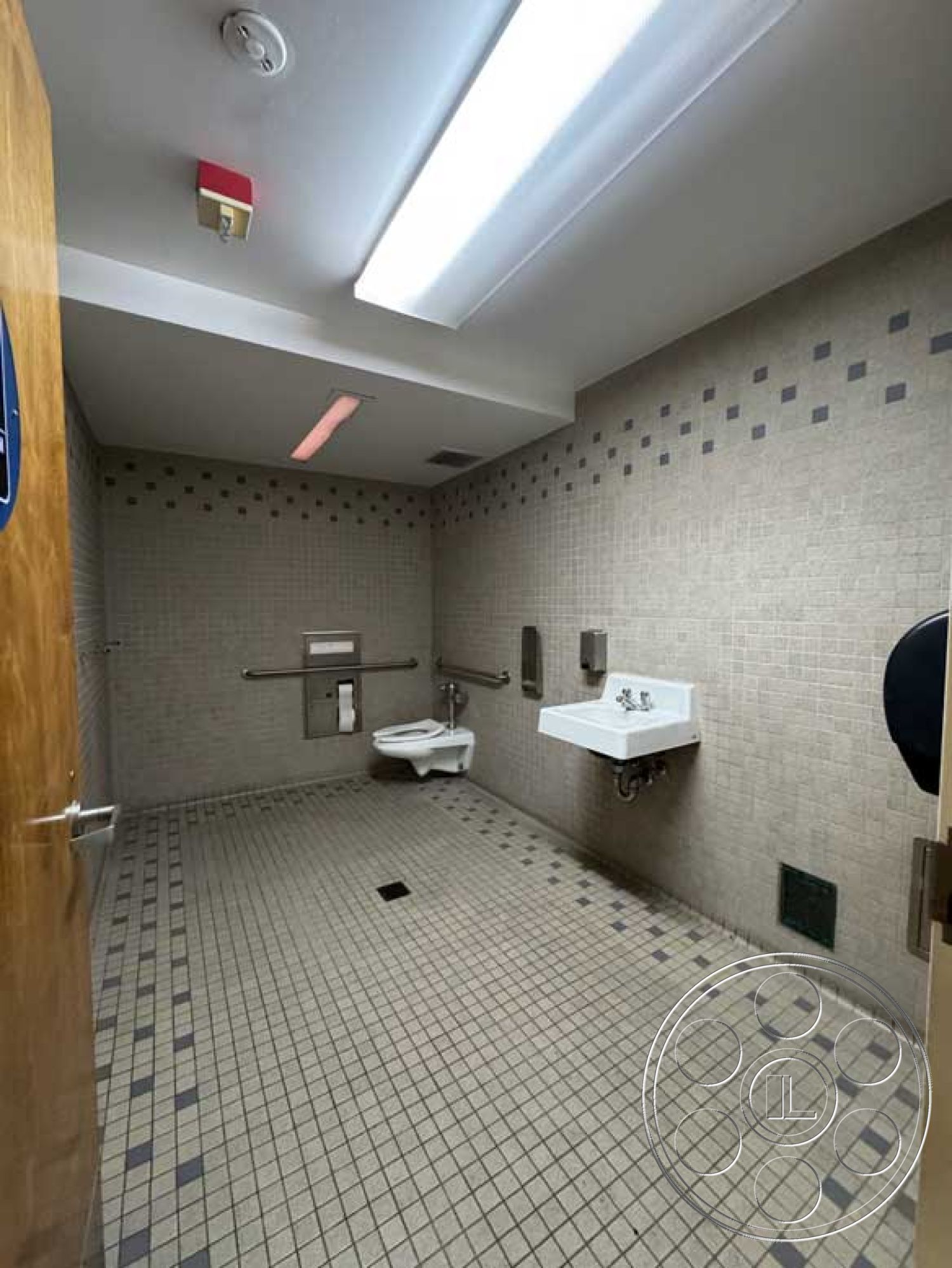 School 3 - ceramic tile flooring, exposed plumbing, gray and white color scheme, interior bathroom, chrome faucet fixtures, LED ceiling lighting, mosaic tile bathroom walls, white wall-mounted sink, toilet with grab bars, flat-panel wooden door, handicap accessible design, square floor drain, tactile signage, non-slip flooring