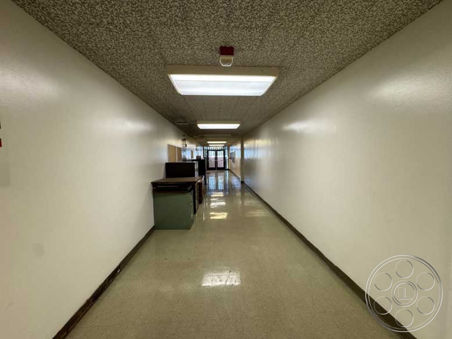 School 3 - commercial space, linear lighting, acoustic ceiling tiles, interior hallway, white painted walls, modern office design, textured ceiling finish, fluorescent ceiling lights, glossy vinyl flooring, long rectangular layout, wall-mounted trash bins, double glass entrance doors