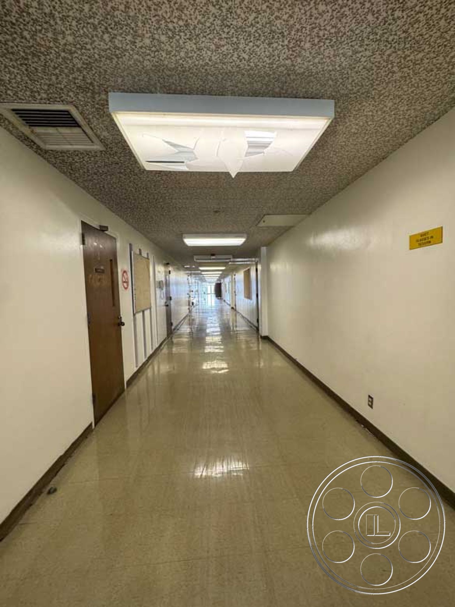 School 3 - neutral color palette, clean lines, wooden door, functional design, commercial space, long corridor, acoustic ceiling tiles, interior hallway, white painted walls, fluorescent ceiling lights, vinyl tile flooring, metal door frames