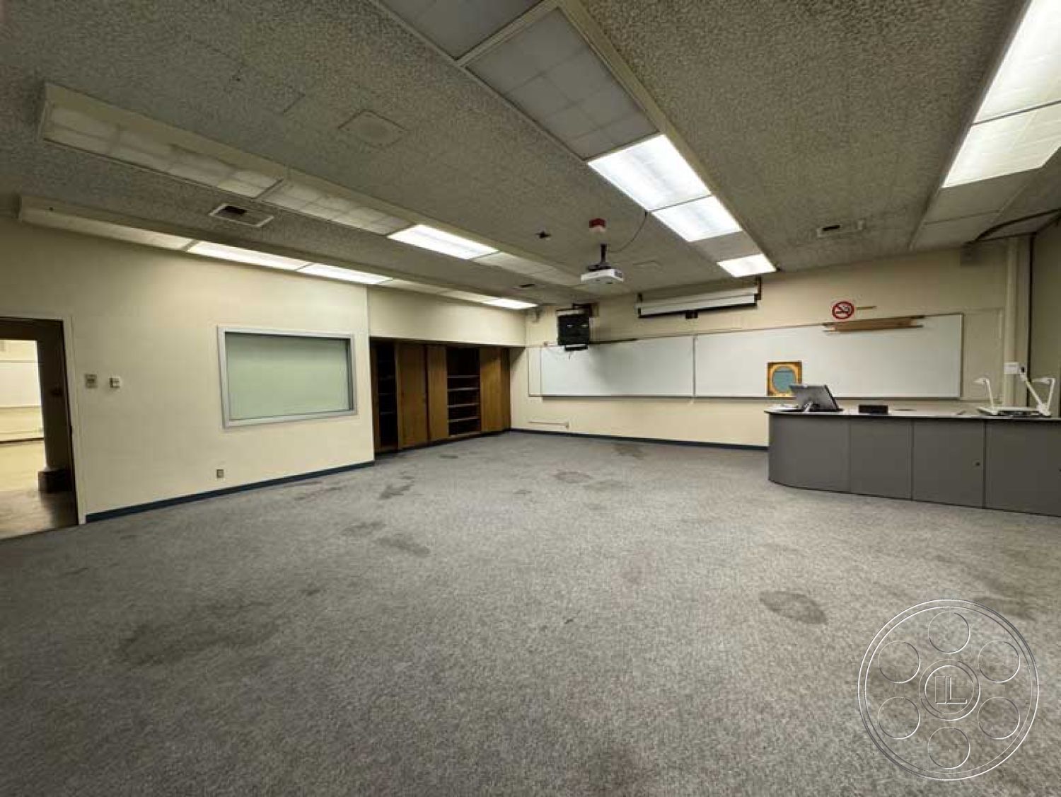 School 3 - acoustic ceiling tiles, white painted walls, built-in shelving units, interior classroom setting, glass window partition, projector mounted on ceiling, carpet classroom flooring, vintage classroom lighting fixtures, teacher's workstation, large whiteboard wall