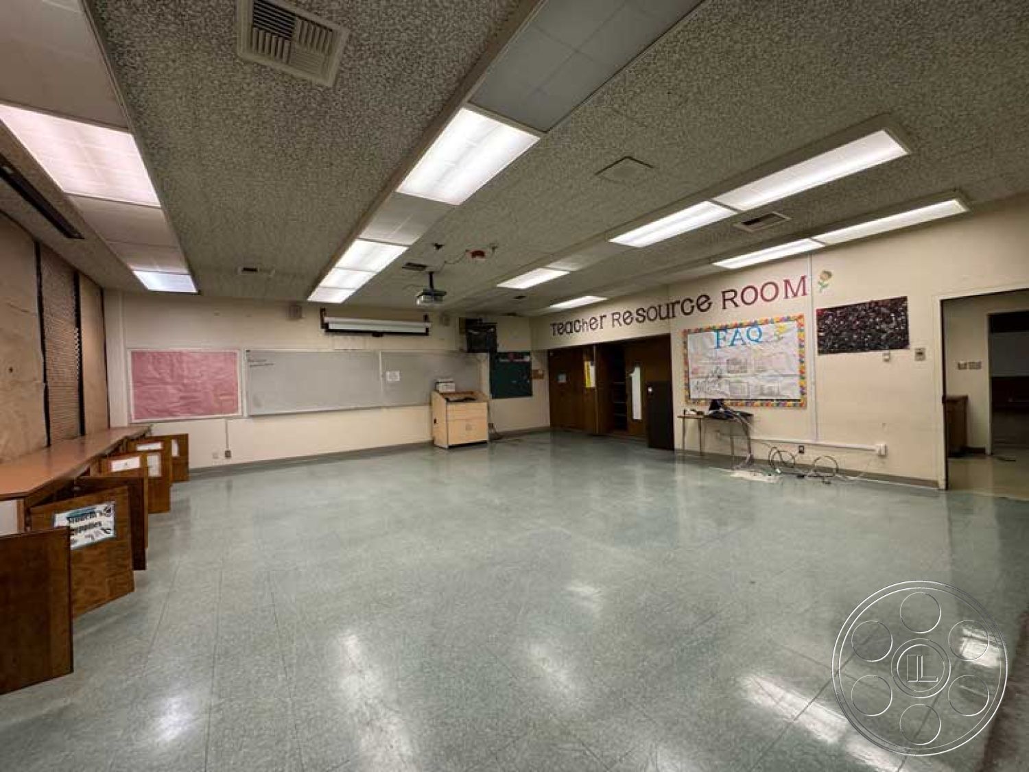School 3 - open floor plan, wood cabinetry, functional workspace, multi-purpose room, projection screen, educational environment, acoustic ceiling tiles, painted drywall walls, vinyl tile flooring, interior classroom space, single-story layout, teacher resource room, standard fluorescent lighting, glass board, colorful bulletin board, architectural details of education spaces