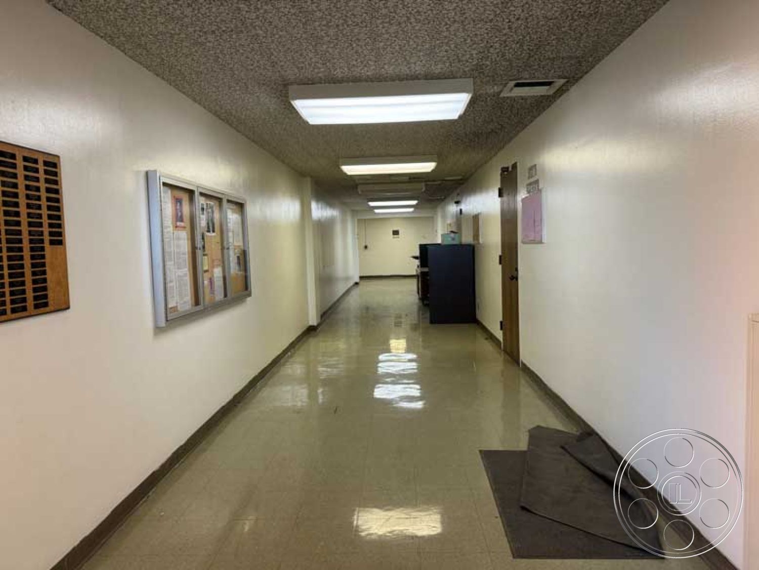 School 3 - acoustic ceiling tiles, wide hallway design, functional office environment, bulletin board wall treatment, polished vinyl corridor flooring, glossy white painted walls, recessed fluorescent lighting, exterior corridor space, administrative hall layout, single wooden office doors, minimalist corridor aesthetic, walled space with artwork display