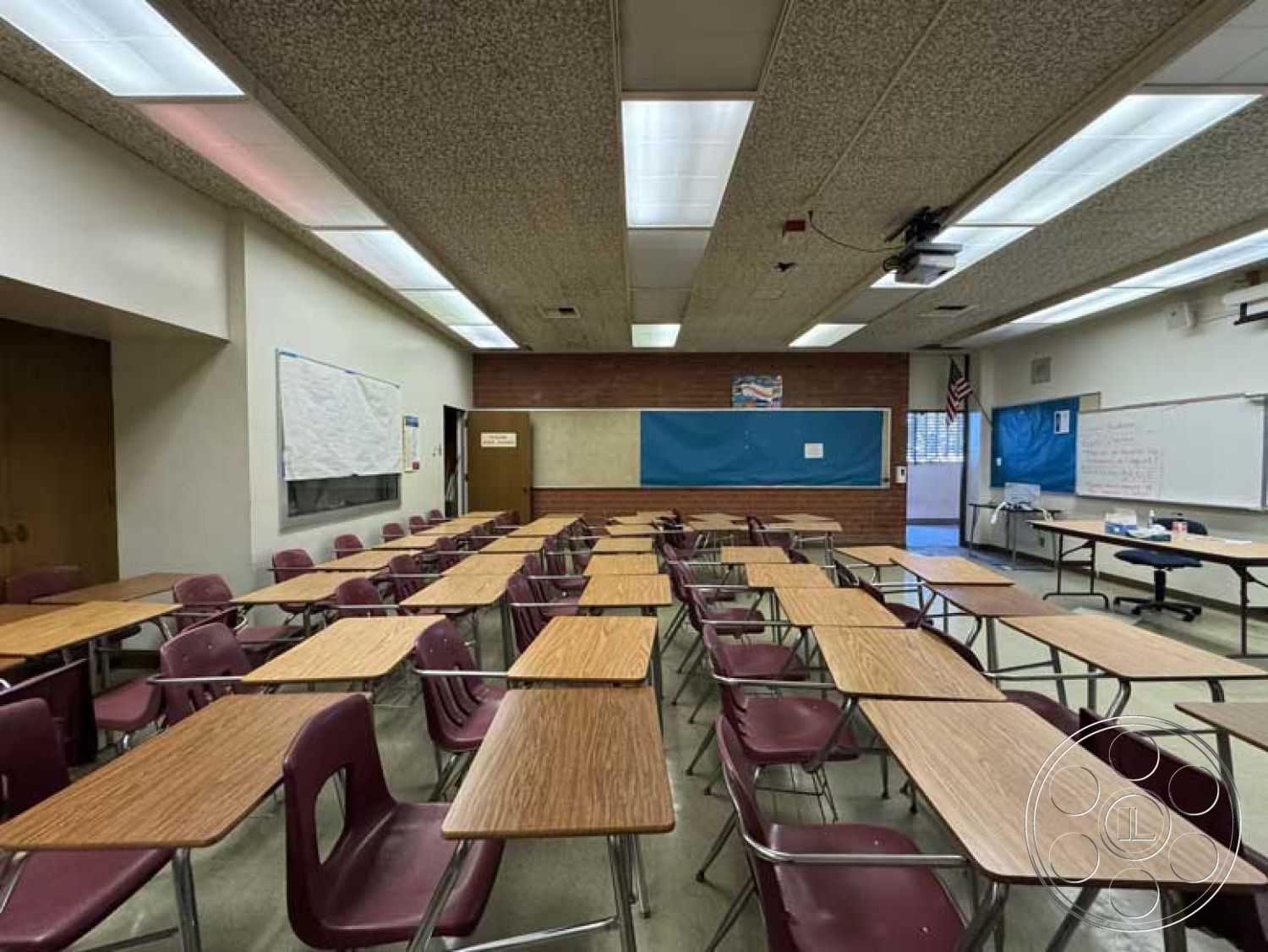 School 3 - brick accent wall, acoustic tile ceiling, vinyl tile flooring, double wooden doors, interior classroom design, projector mounted ceiling, fluorescent lighting panels, laminate wood classroom desks, stackable plastic student chairs, painted drywall bulletin boards, control panel for AV equipment, wall-mounted chart paper, high-traffic classroom environment, traditional educational setting, group seating arrangement, colorful educational displays, window-covered walls, functional teaching space, multifunctional classroom layout, urban school environment, teacher's workstation in classroom