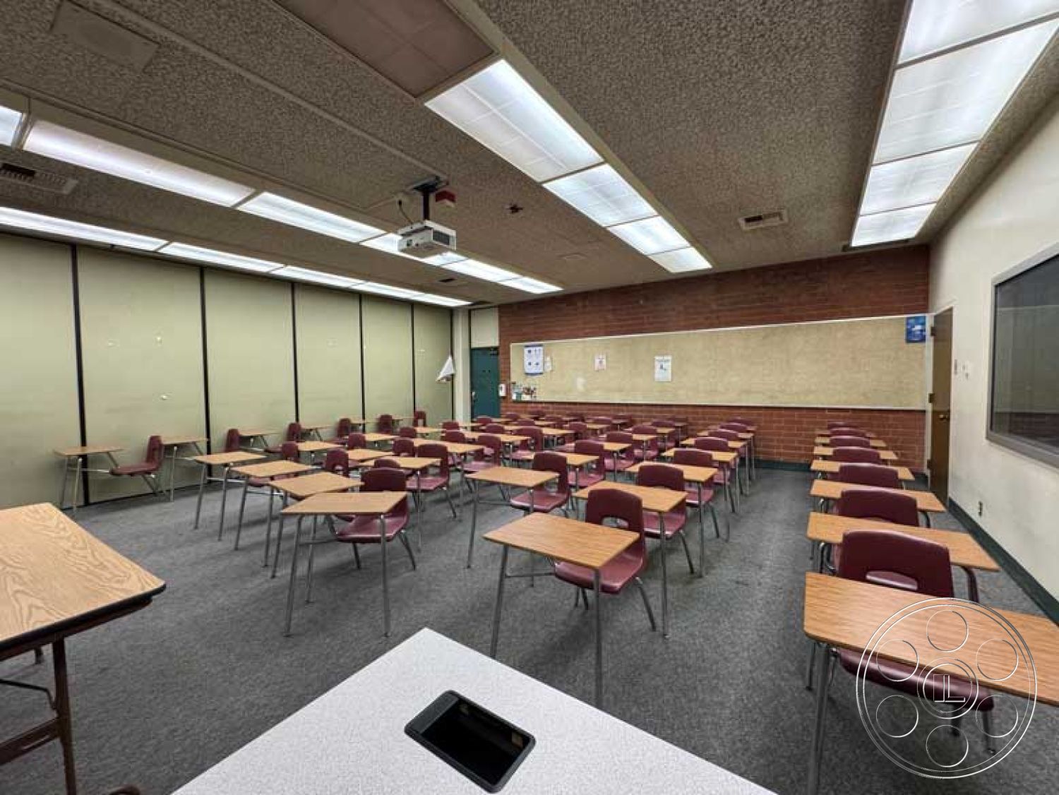 School 3 - neutral color palette, exposed brick wall, chalkboard wall, organized workspace, educational setting, fluorescent ceiling lights, textured ceiling tiles, vinyl tile flooring, interior classroom design, acoustic ceiling design, wooden student desks, functional classroom layout, projector mounted ceiling, drywall partition, plastic seat chairs, double-pane windows, open classroom environment