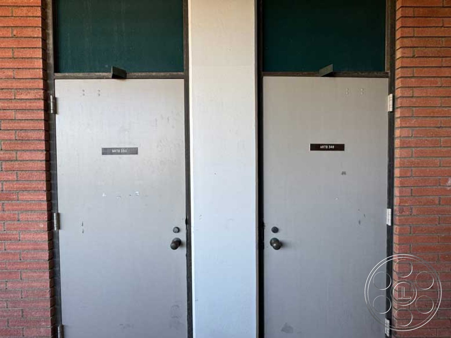 School 3 - double door entry, modern architectural details, brick exterior wall, painted metal doors, grey door finish, green glass transom window, industrial-style entrance, symmetrical door layout, label plates on doors, exterior building access, urban college campus setting, interior door frames, minimalistic door handles, brick and metal construction