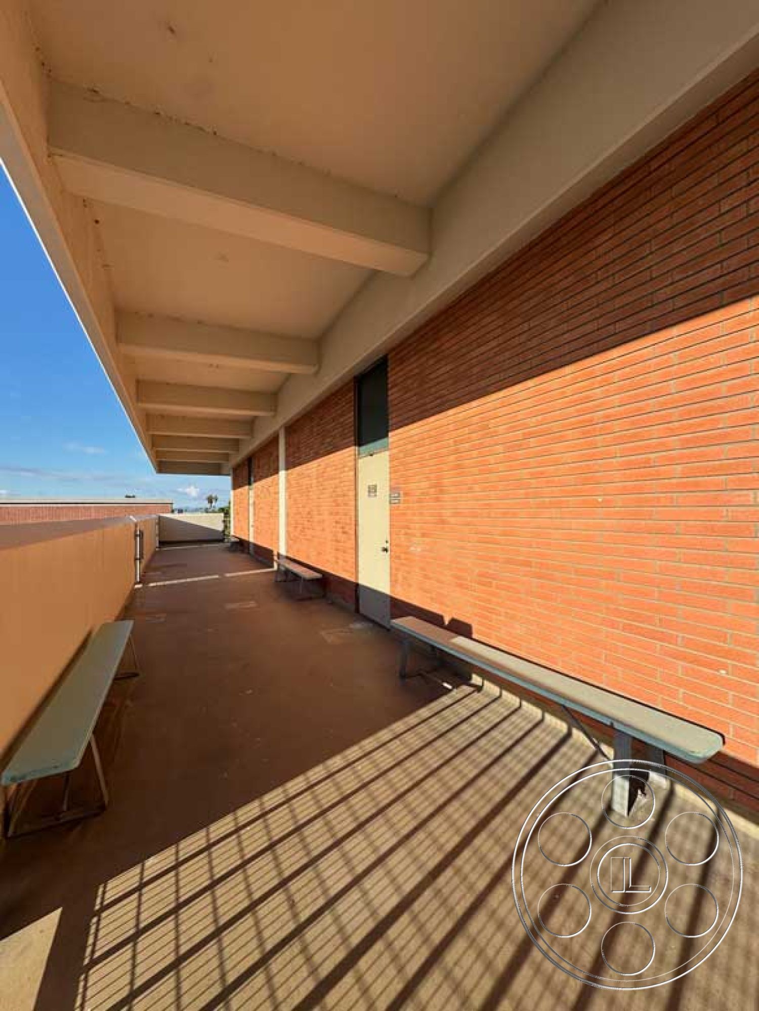 School 3 - neutral color palette, minimalist design elements, urban setting, brick facade, shaded seating area, sunlit exterior, industrial style architecture, exterior brick walls, exposed concrete ceiling beams, concrete walkway flooring, metal bench seating, rectangular open corridor, modern architectural detail, sustainable materials use, clear sky backdrop