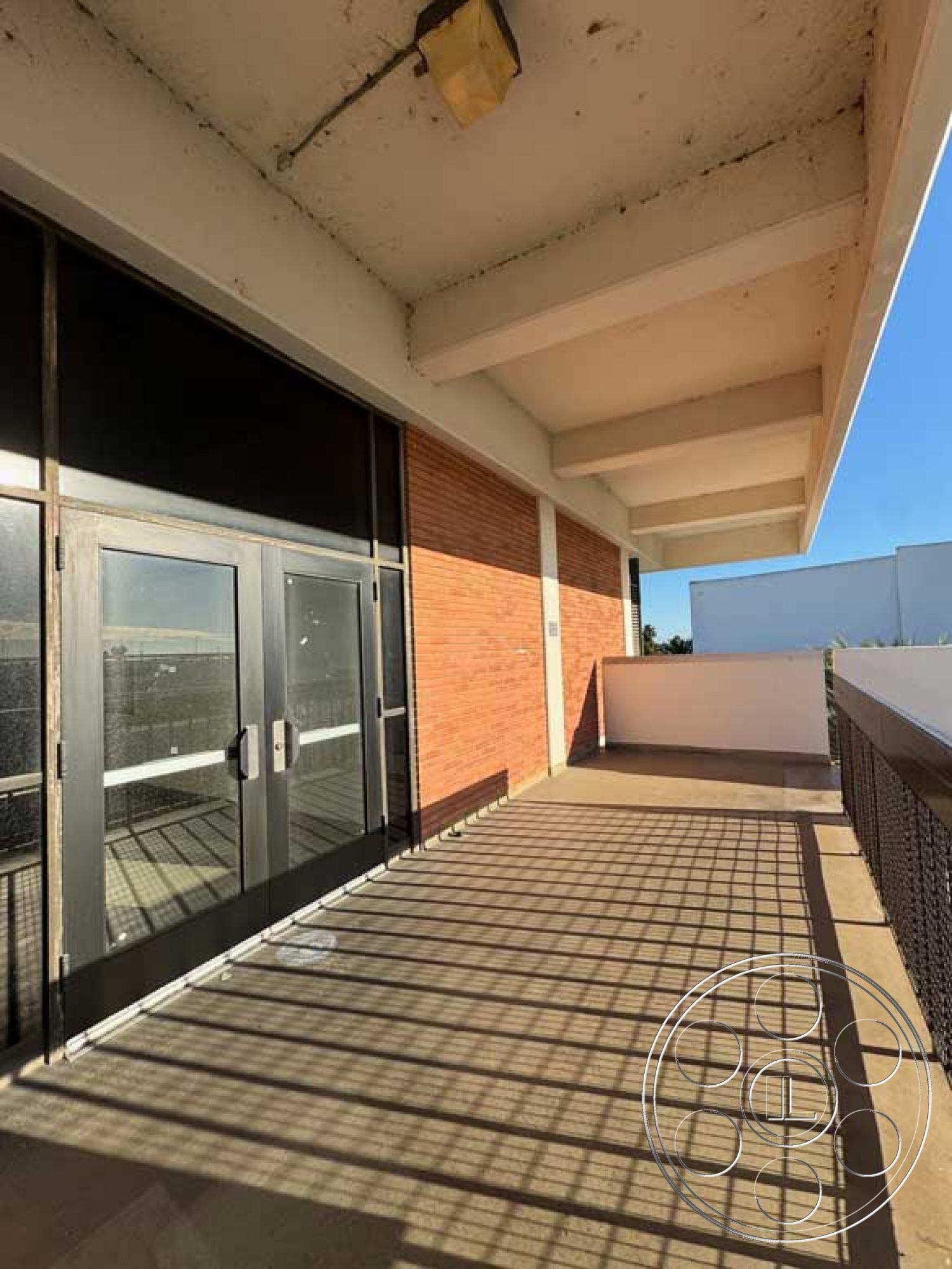 School 3 - exposed brick wall, steel railing, glass double doors, modern architectural elements, flat roof exterior, shadow patterns on floor, concrete balcony floor, commercial style entrance, outdoor urban setting
