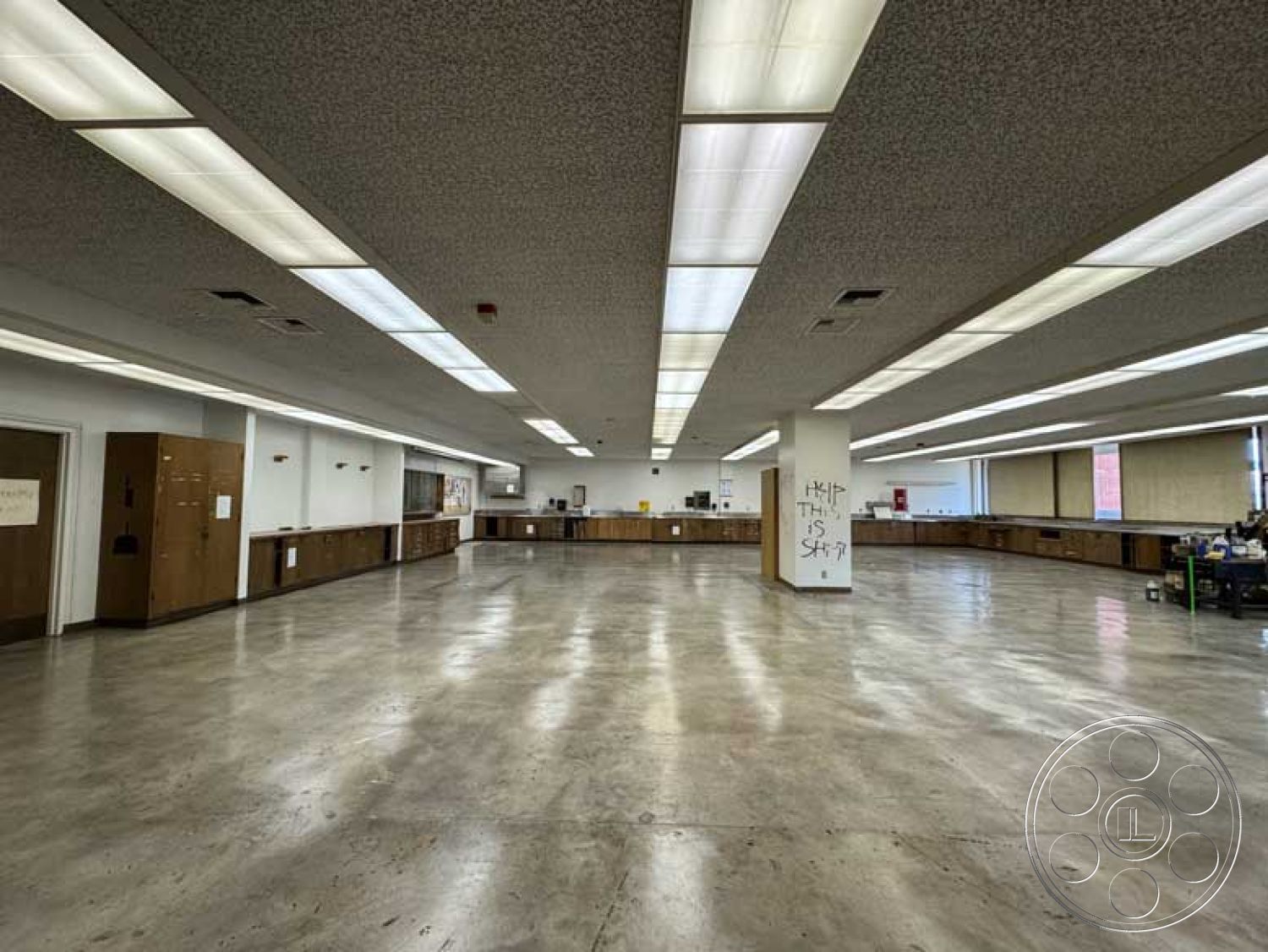 School 3 - textured wall surfaces, multipurpose room, open floor plan layout, minimalist architectural style, exposed concrete flooring, urban setting interior, acoustic tile ceiling, functional workspace design, neutral color palette walls, utilitarian design elements, large window openings, wood cabinetry installations, linear fluorescent lighting fixtures, commercial interior space, double-door entry points, public service environment