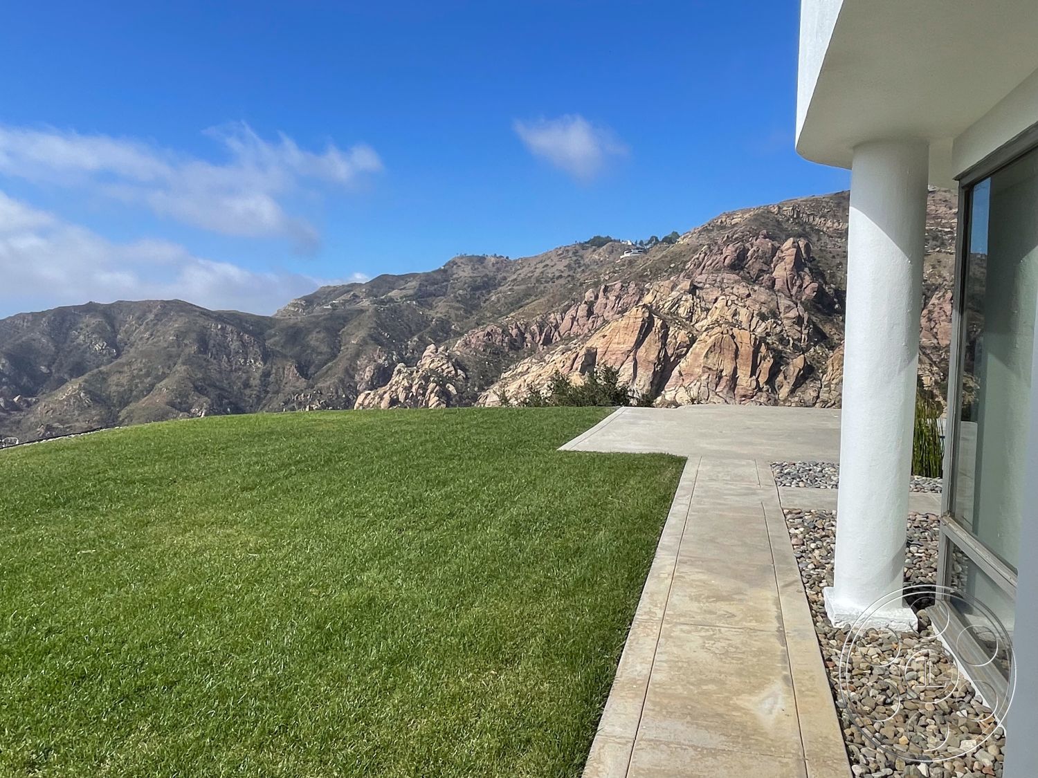 Modern 56 - modern architectural style, smooth concrete finish, mountain view setting, exterior concrete patio floor, sloped hillside location, exterior grass lawn, concrete walkway with decorative stones, landscape with natural rock formations