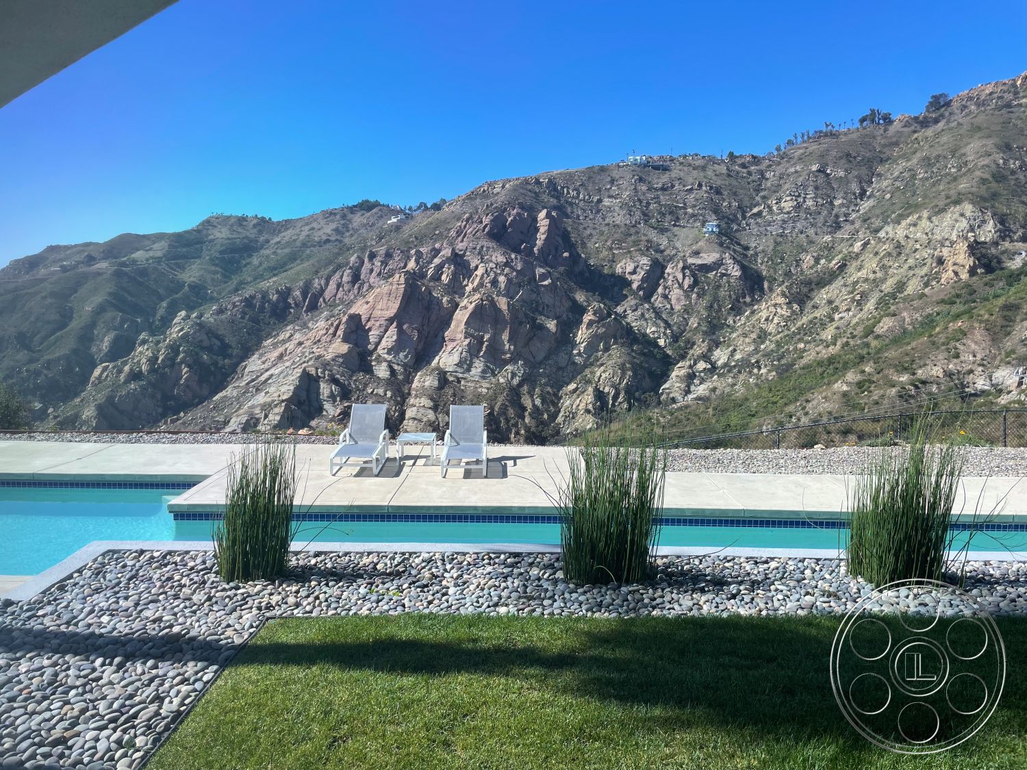Modern 56 - grass lawn, mountain view, clear blue sky, concrete pool deck, rectangle swimming pool, concrete patio flooring, exterior pool area, pebble stone landscaping, modern outdoor chaise lounges, desert hillside setting