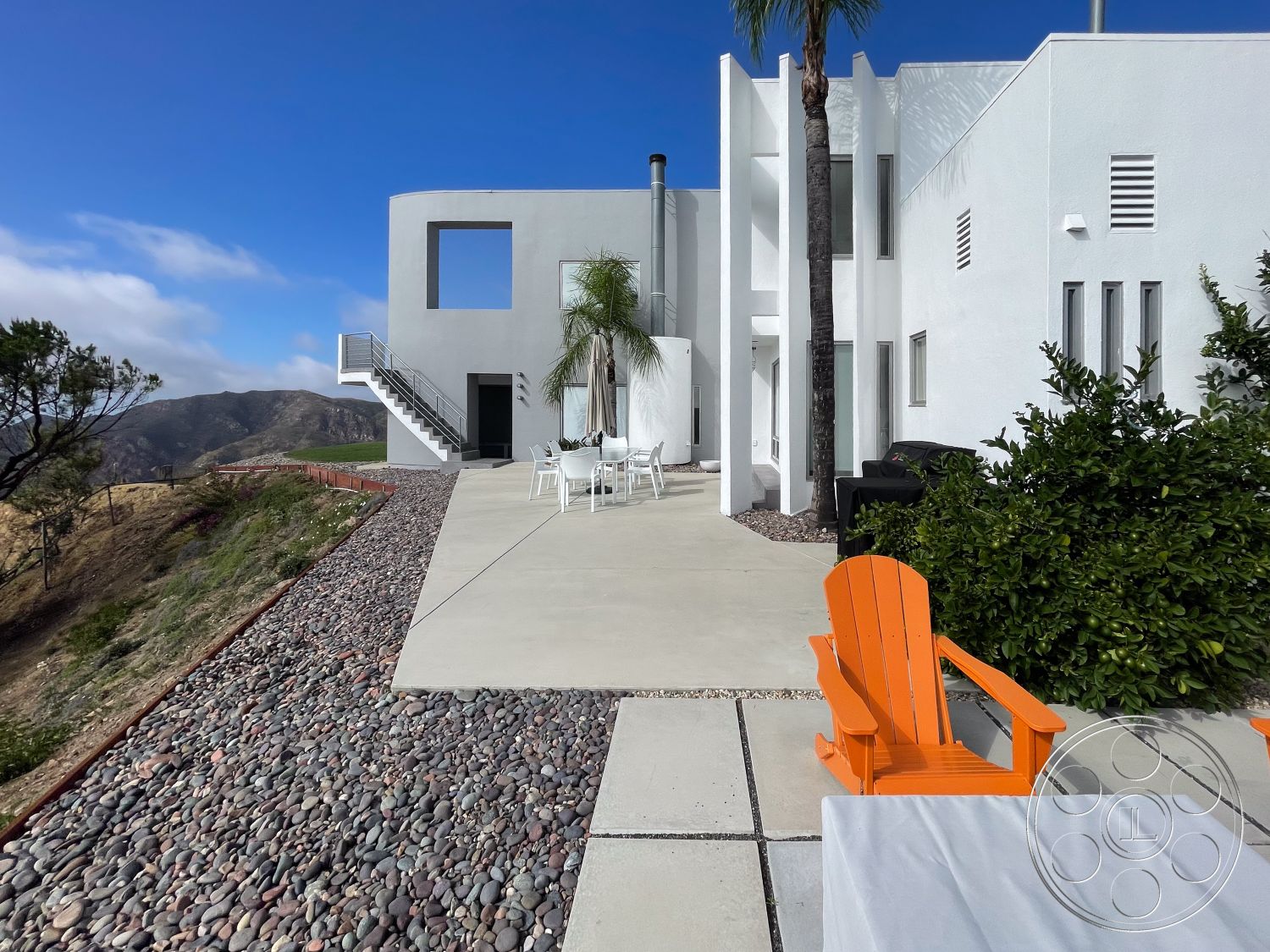 Modern 56 - exterior, white stucco walls, modern architecture, minimalist design, open concept layout, floor-to-ceiling windows, outdoor dining area, mountain view setting, landscaped garden area, concrete patio flooring, floating stairs, rectangular patio, pebble stone border, orange adirondack chairs
