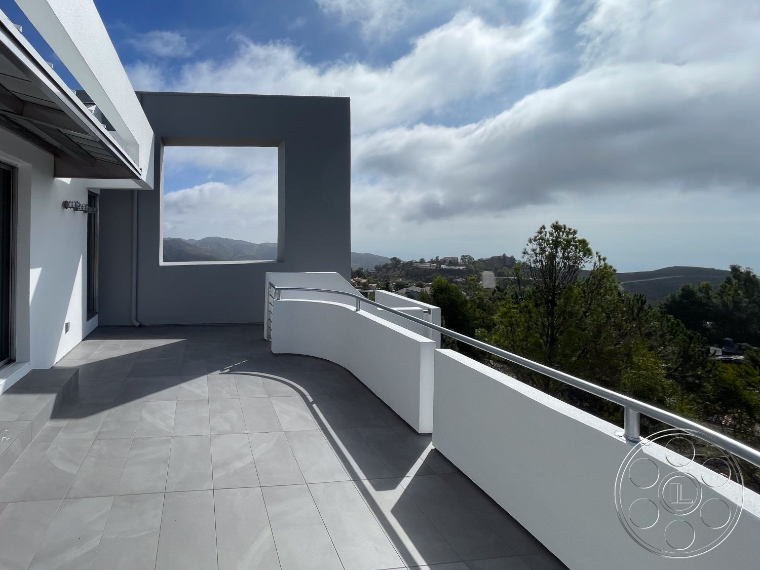 Modern 56 - exterior, white stucco walls, open space, minimalist design elements, natural surroundings, metal railing, floor-to-ceiling windows, modern architectural style, mountain view, grey concrete flooring, contemporary outdoor setting, large rectangular balcony, curved balcony edge, sweeping sky backdrop