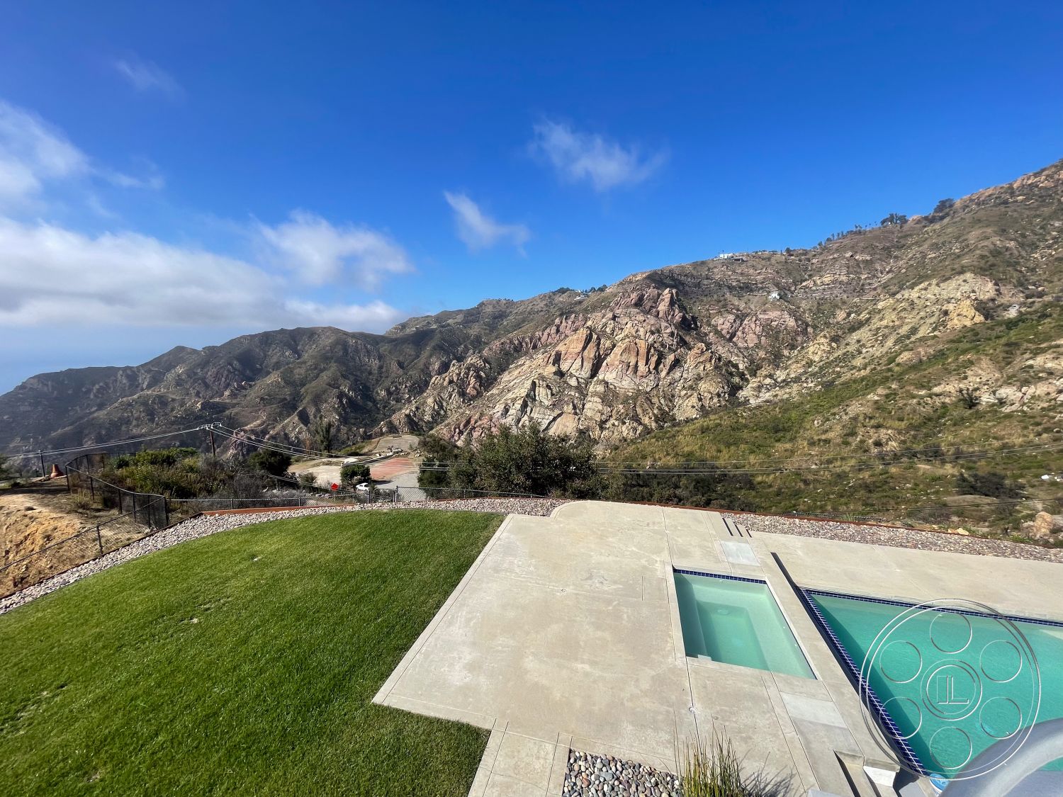 Modern 56 - rectangular swimming pool, mountain view setting, modern minimalist architecture, exterior concrete pool deck, infinity pool with sleek lines, landscaped backyard with natural grass, surrounding rocky hillside landscape, concrete patio floor adjacent to pool, landscape gravel border around lawn, open outdoor space with expansive views