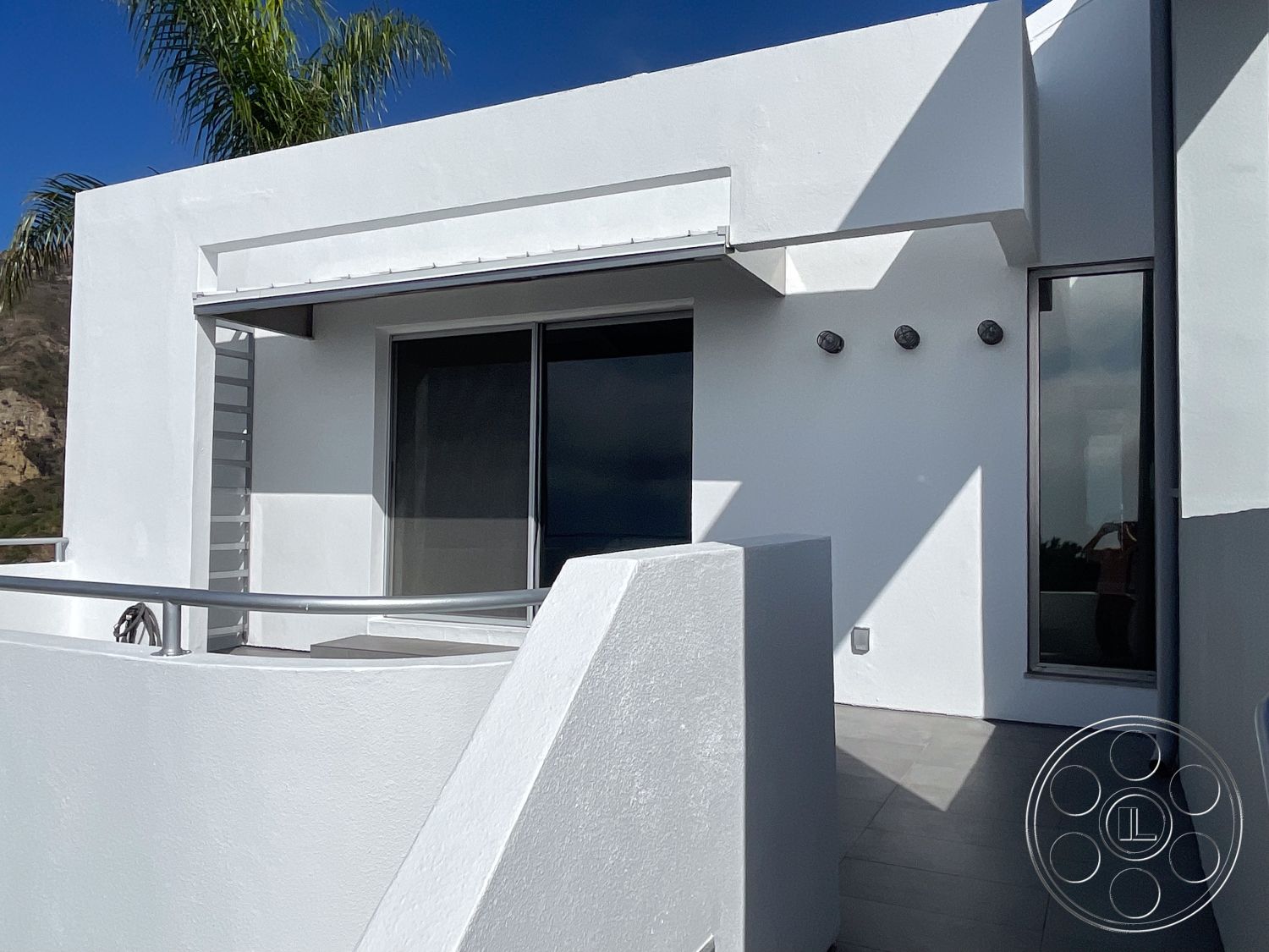 Modern 56 - exterior, white stucco walls, minimalist design elements, horizontal lines, sliding glass door, modern architectural style, aluminum railing, outdoor lighting fixtures, smooth stucco finish, flat roof design, palm tree landscaping, large glass window, concrete terrace flooring, landscaped hillside setting, panoramic mountain view, contemporary balcony