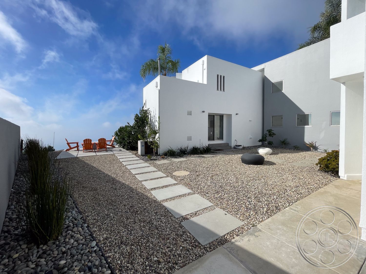 Modern 56 - exterior, white stucco walls, minimalist design, sliding glass doors, modern architectural style, desert landscape, hillside location, wooden Adirondack chairs, concrete patio floor, sunny urban setting, pebble landscape stones, rectangular stepping stones, planting beds with drought-resistant plants, concrete outdoor table, outdoor sculptural stone