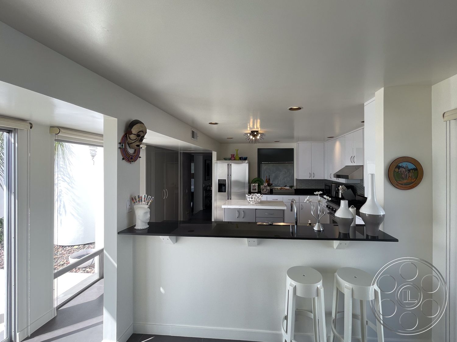 Modern 56 - hardwood flooring in dining area, stainless steel appliances in kitchen, interior kitchen with black granite countertops, white cabinetry with modern flat-panel doors, glass sliding doors for natural light, light-colored painted walls, open concept layout connecting kitchen and living space, round white bar stools at kitchen island, textured ceiling with recessed lighting, decorative wall art and cultural accents, minimalist decor with simple shapes, contemporary kitchen faucets, sliding glass windows offering outdoor view, modern backsplash tile behind kitchen sink