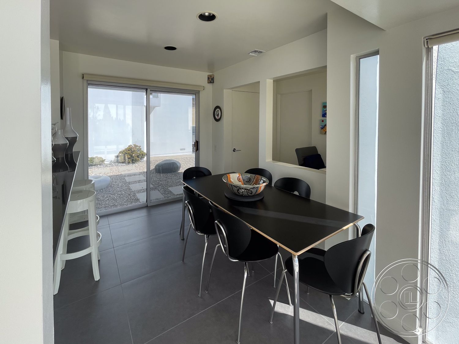 Modern 56 - neutral color palette, natural light, open concept layout, indoor-outdoor flow, sliding glass doors, ceramic tile flooring, framed wall art, black dining table, interior dining area, modern minimalist design, granite kitchen countertops, white painted walls, contemporary ceiling lights, metal chair design, decorative bowl centerpiece, landscaped stone patio