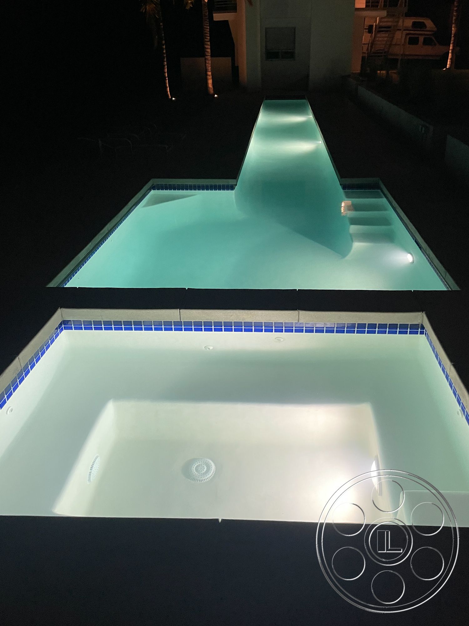 Modern 56 - concrete pool deck, outdoor relaxation space, rectangular infinity pool, desert home setting, spa with tile surround, blue mosaic tile border, illuminated pool steps, exterior night lighting, landscaped pool area, dark concrete patio floor