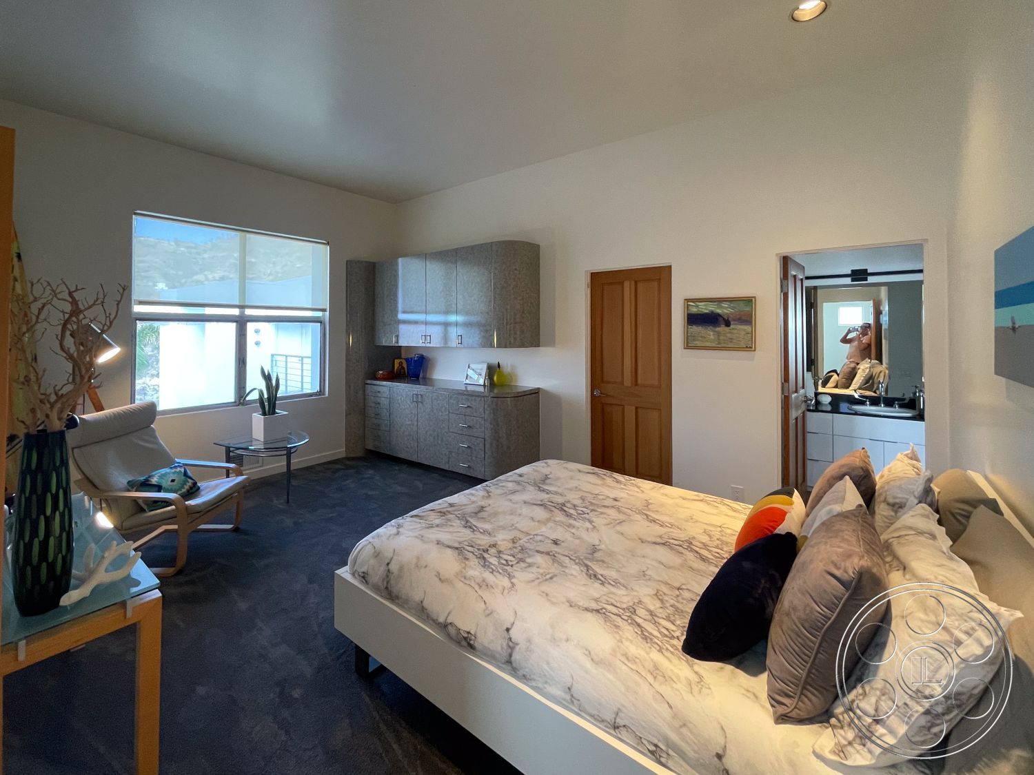 Modern 56 - neutral wall colors, open space layout, carpet flooring, artwork on wall, bright natural lighting, potted plant decor, decorative bedside table, interior bedroom, glass window treatments, marble bedspread, wooden bedroom door, modern dresser cabinetry, soft seating armchair, bathroom access door