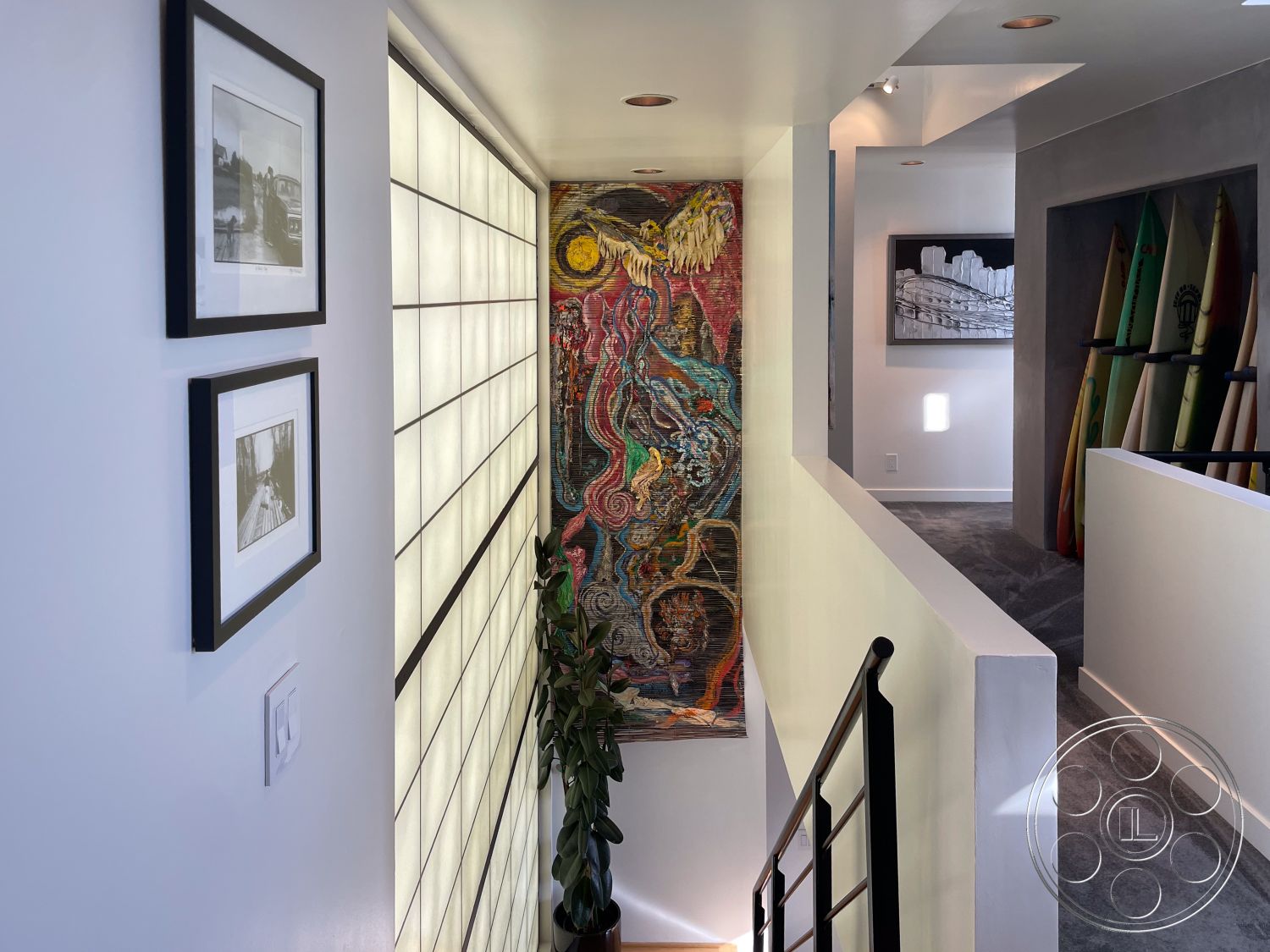 Modern 56 - minimalist decor, framed black and white photographs, contemporary architectural style, colorful abstract wall art, interior hallway with white painted walls, glass block wall feature, dark metal stair railings, carpeted flooring in hallway, soft natural lighting from glass wall, open layout with modern design, multi-functional space with artistic touches, surfer-themed wall display with surfboards, textured wall adjacent to hallway, inviting residential setting