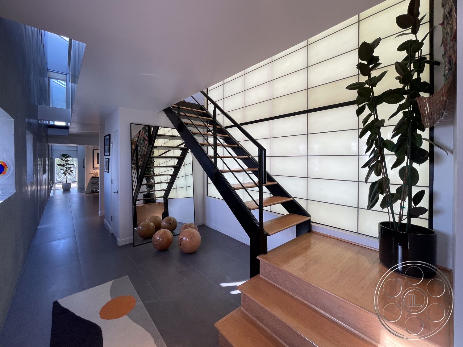 Modern 56 - floor-to-ceiling glass windows, interior hall with concrete wall treatment, interior open staircase with wooden treads and steel railings, exposed wooden ceiling beams in modern design, rectangular glass wall panels providing natural light, porcelain tile flooring in entryway, minimalist design with decorative indoor plants, modern art displayed on wall, geometric area rug with abstract patterns, curved wall feature creating visual interest