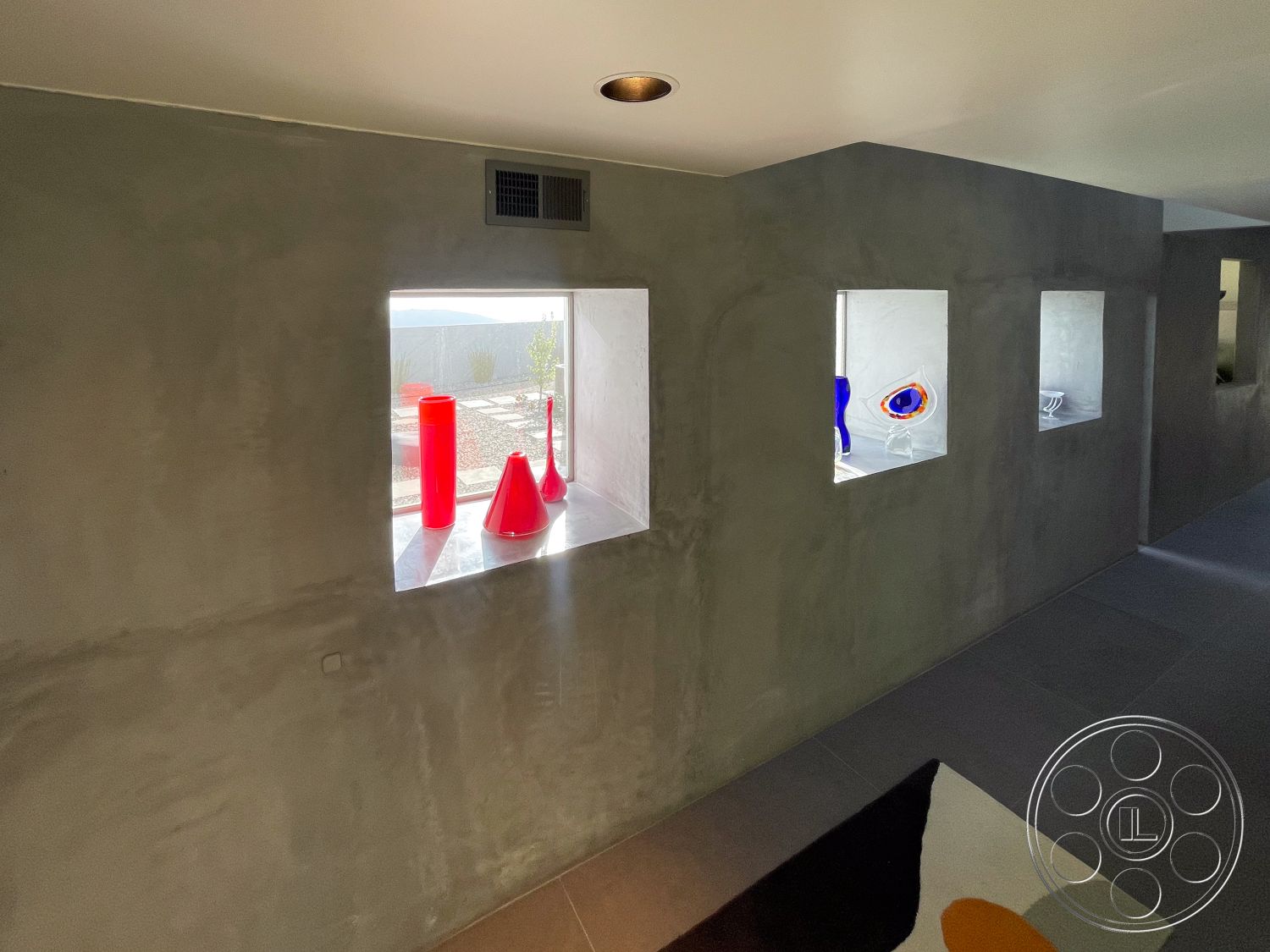 Modern 56 - neutral color palette, contemporary architectural style, exposed concrete walls interior, polished concrete flooring interior, textured plaster finish interior, square window openings with glass accents, simple geometric forms in design, natural light through window cutouts, minimalist aesthetic with functional design, soft lighting from recessed ceiling fixtures, modern art display on window ledges, open floor plan with sleek lines