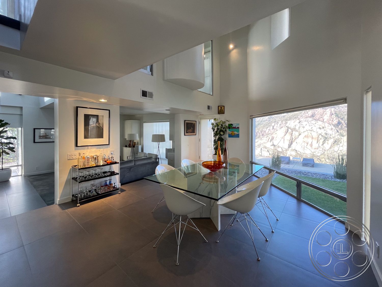 Modern 56 - open-concept layout, contemporary lighting fixtures, natural light flooding the space, smooth white painted walls, interior dining room with glass dining table, sleek white chairs with metal legs, dark ceramic tile flooring, large floor-to-ceiling windows with mountain view, modern bar cart with glassware, minimalist decor with abstract art, stylish indoor greenery, high ceilings with angular architecture